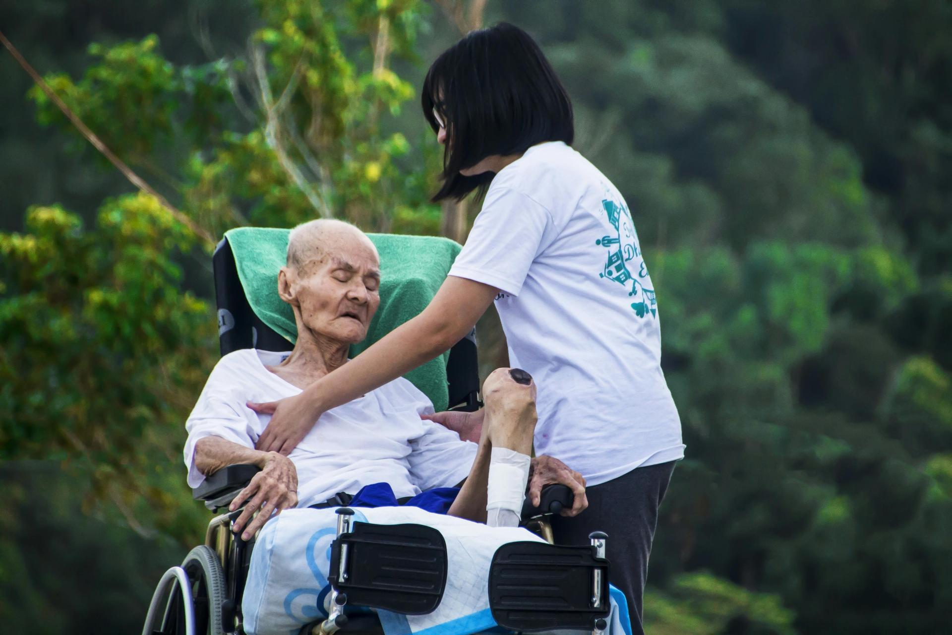 A caregiver's hand gently rests on the hand of an elderly person in a quiet domestic setting