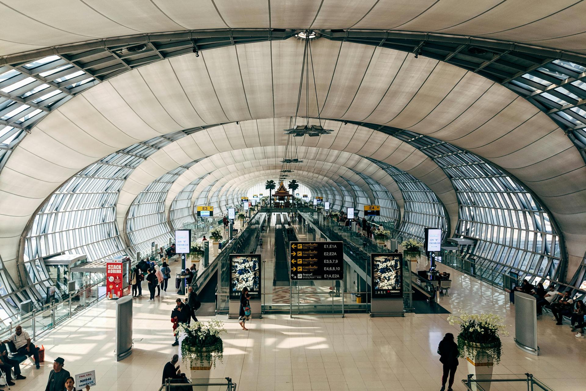 A wide overhead view of travellers moving through an international airport terminal with suitcases in tow.