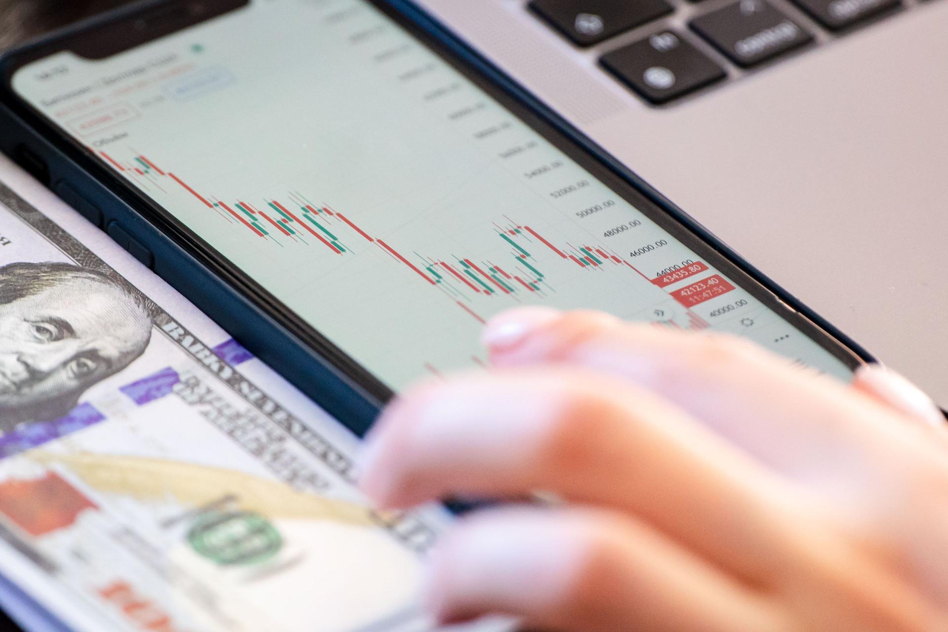 A smartphone screen showing live financial data resting on a US dollar bill, illustrating mobile finance and digital lending.