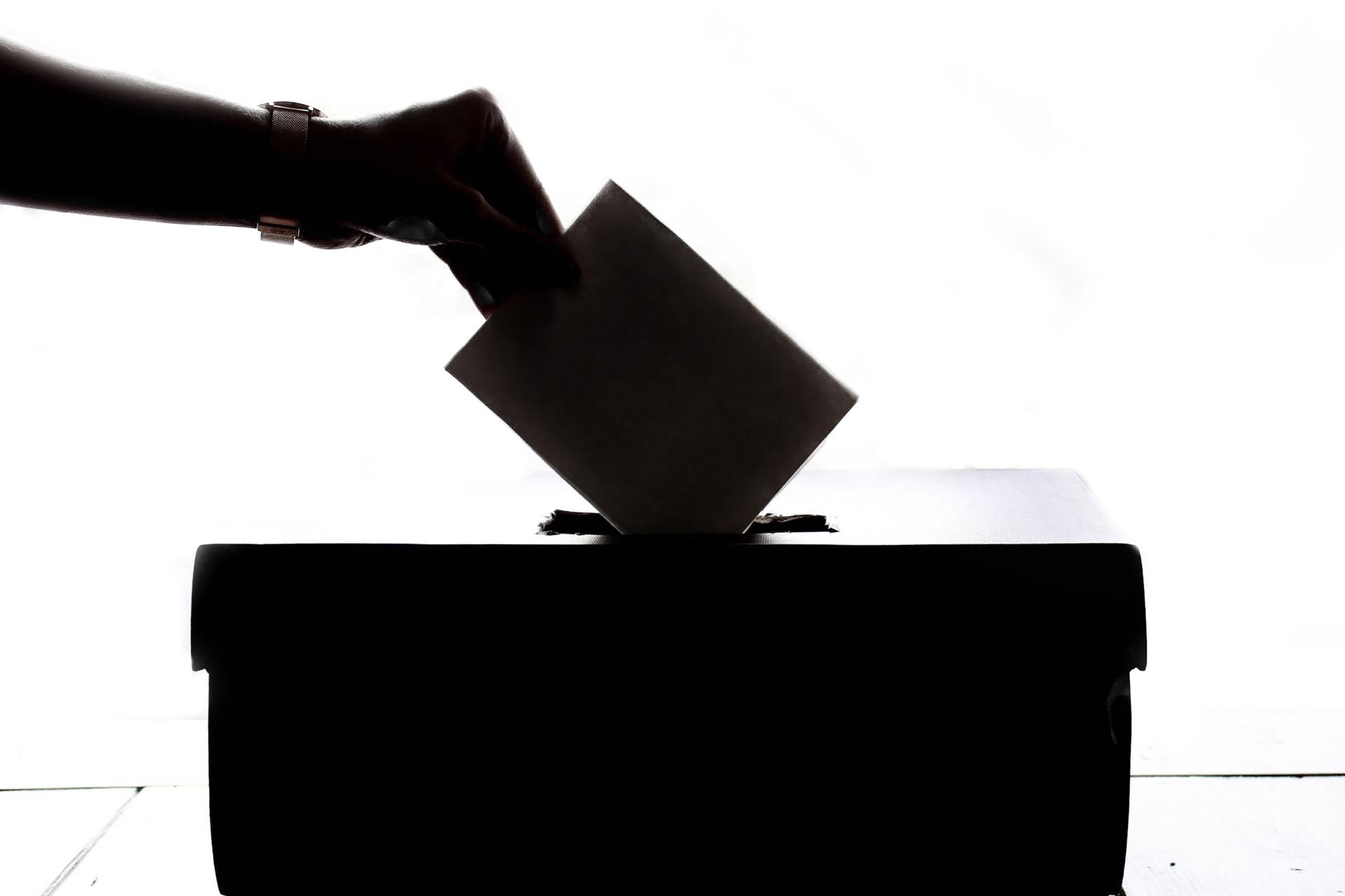 A hand placing a ballot paper into a wooden ballot box, symbolising voting and democratic participation