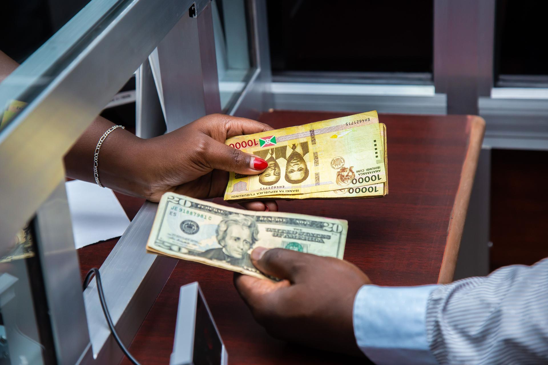 Hands exchanging cash banknotes over a currency exchange counter, illustrating money transfers and diaspora remittances.