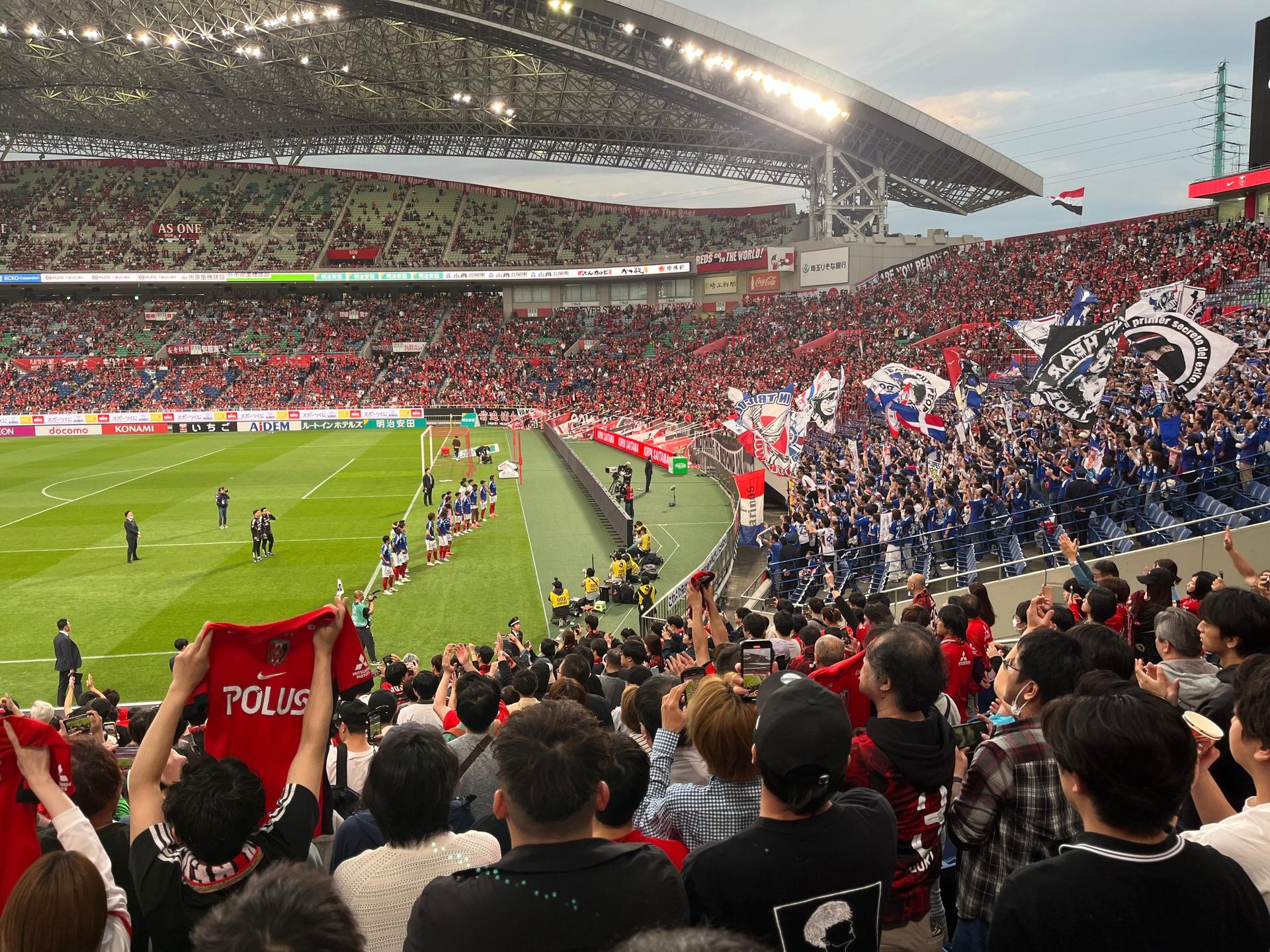 A packed football stadium filled with enthusiastic fans waving and cheering during a match.