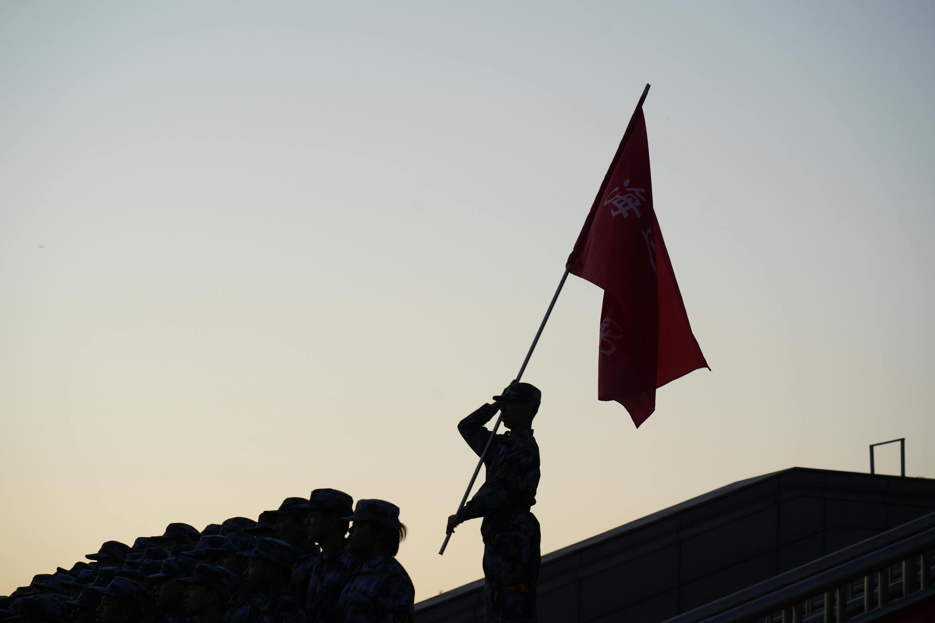 Silhouette of a soldier saluting beside a flag at sunset, symbolising military service and front-line duty