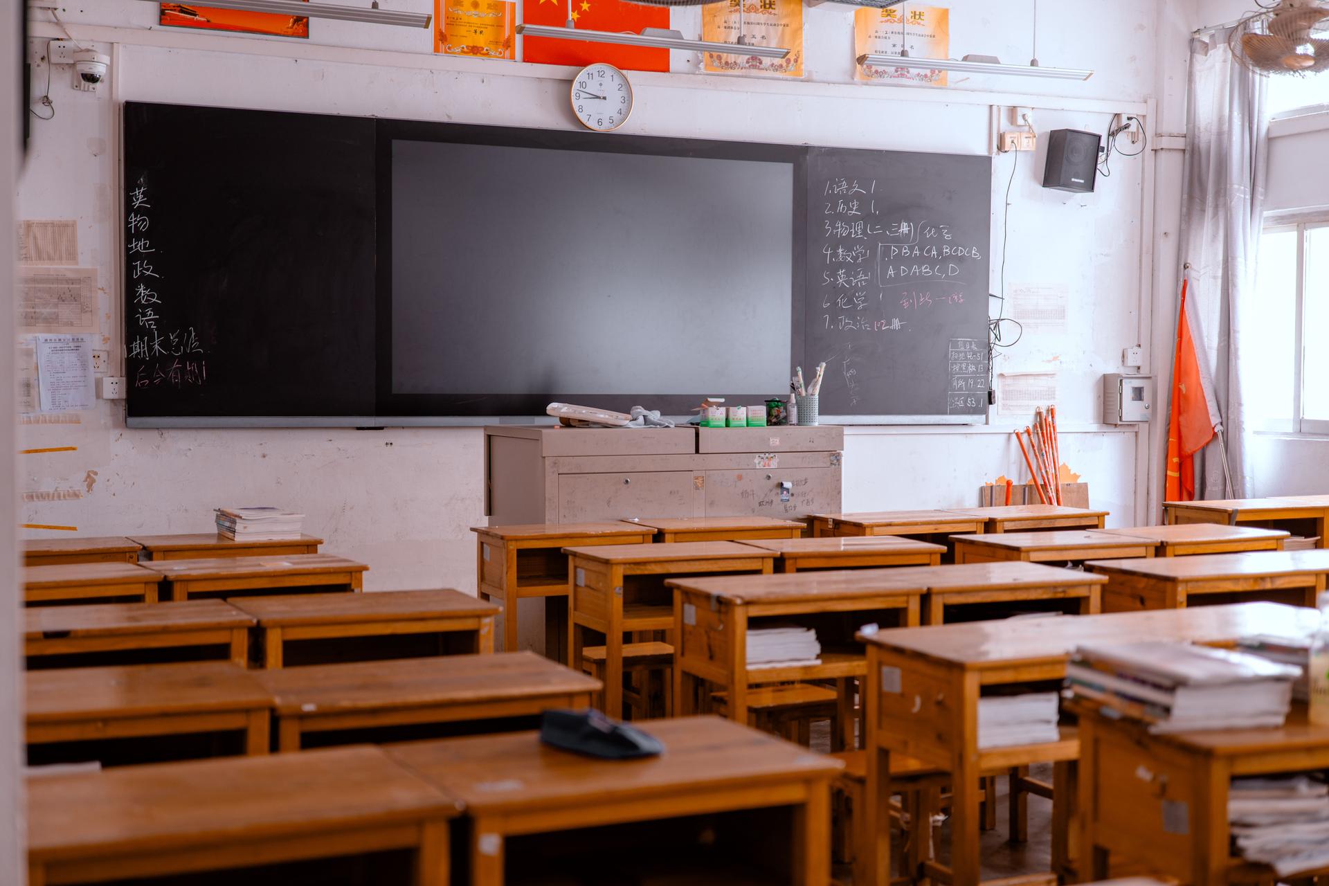 Rows of empty wooden desks and chairs facing a blackboard in a deserted classroom