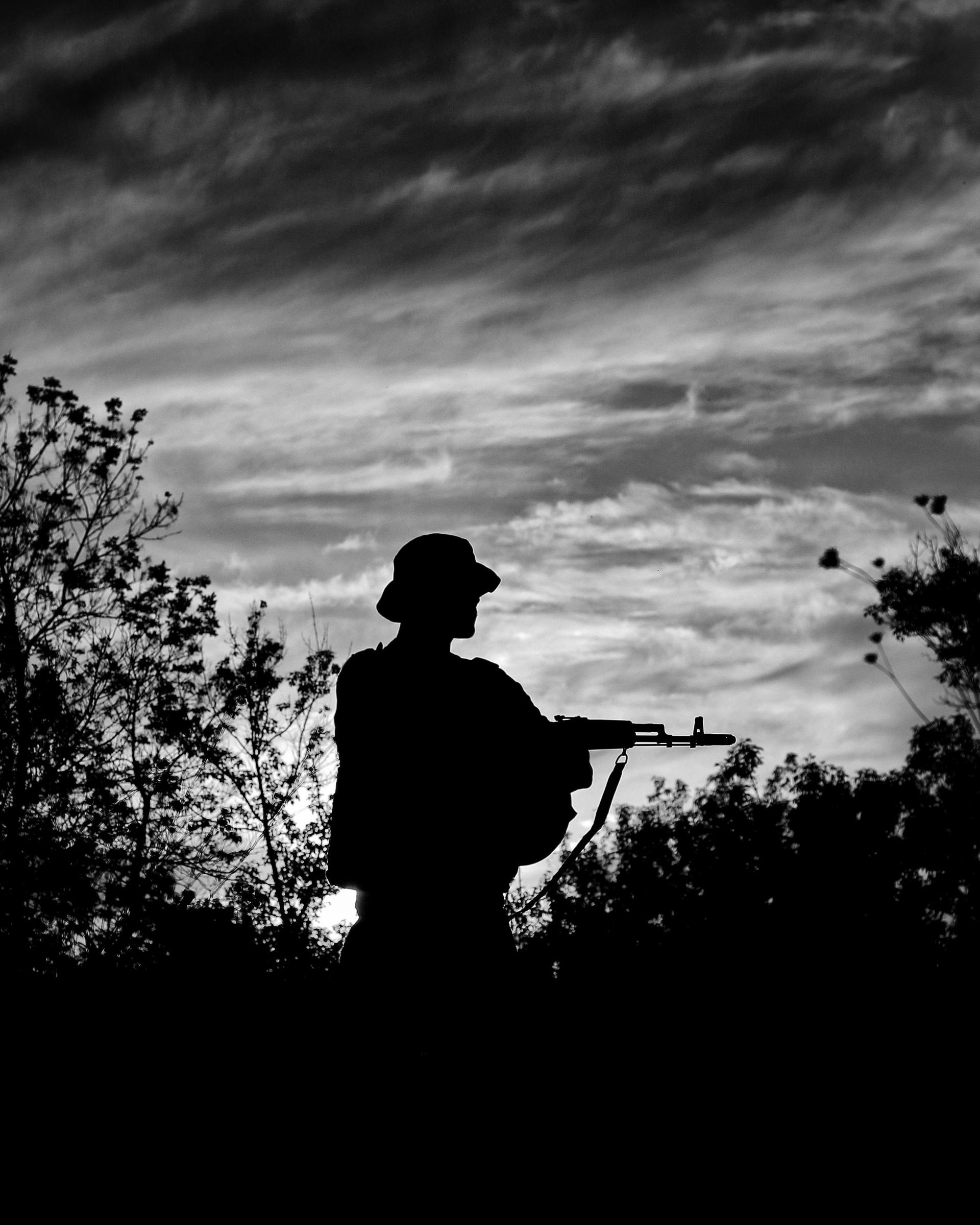 Silhouette of a lone soldier holding a rifle against a dramatic twilight sky in a forest