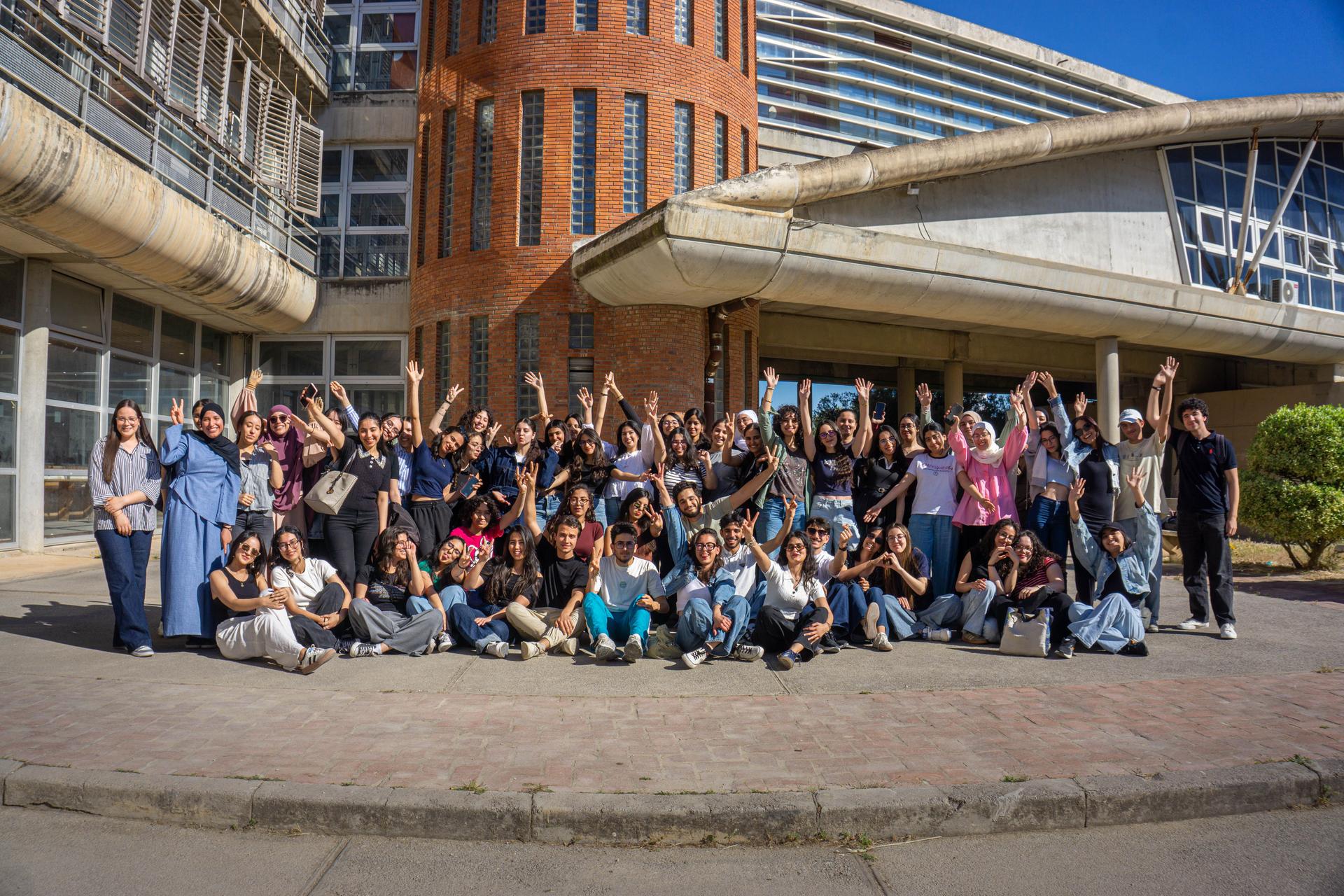 A diverse group of international university students celebrating together outside a modern campus building.