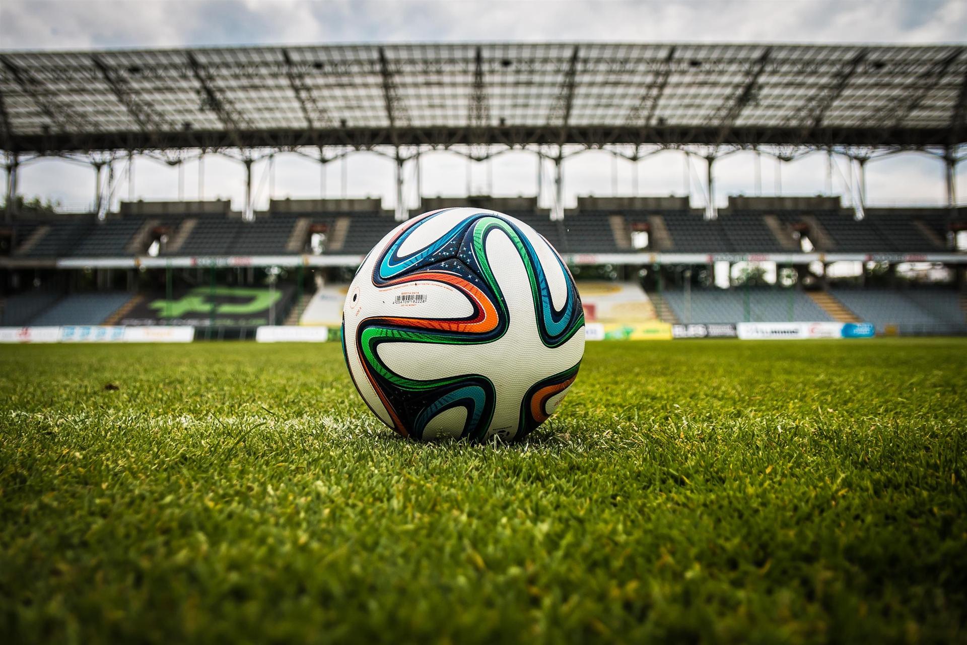 A football resting on the floodlit grass of a stadium pitch in the moments before kick-off.