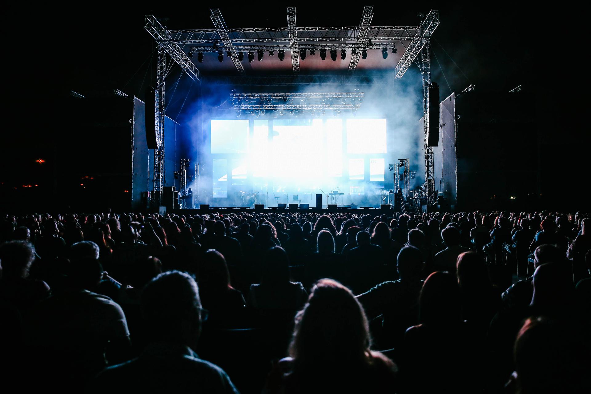 A large outdoor concert crowd enjoying live music under vibrant stage lights at night, evoking a Kenyan diaspora Mugithi show in the United States.