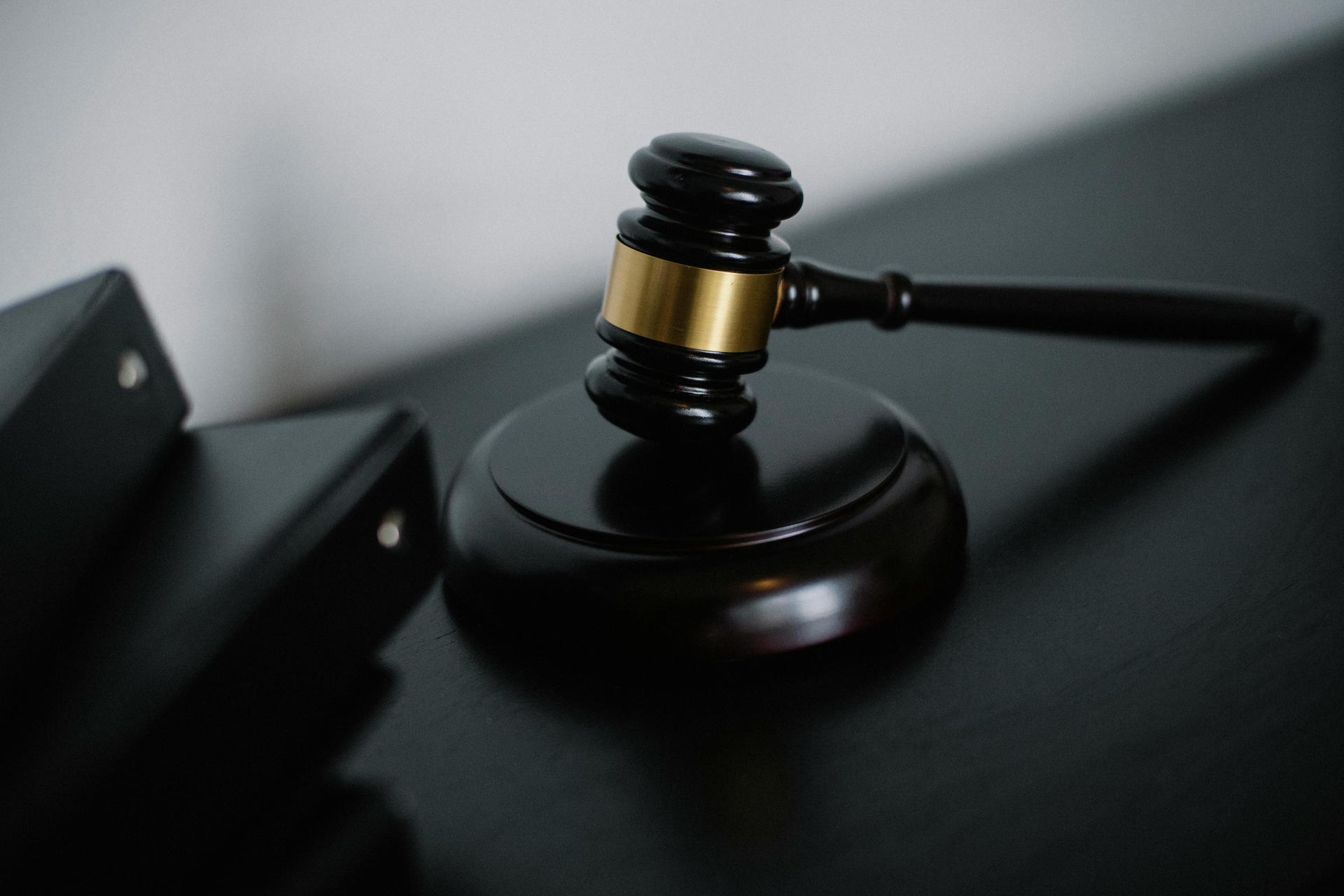 A wooden judge's gavel rests on a desk beside document folders, evoking a courtroom ruling.