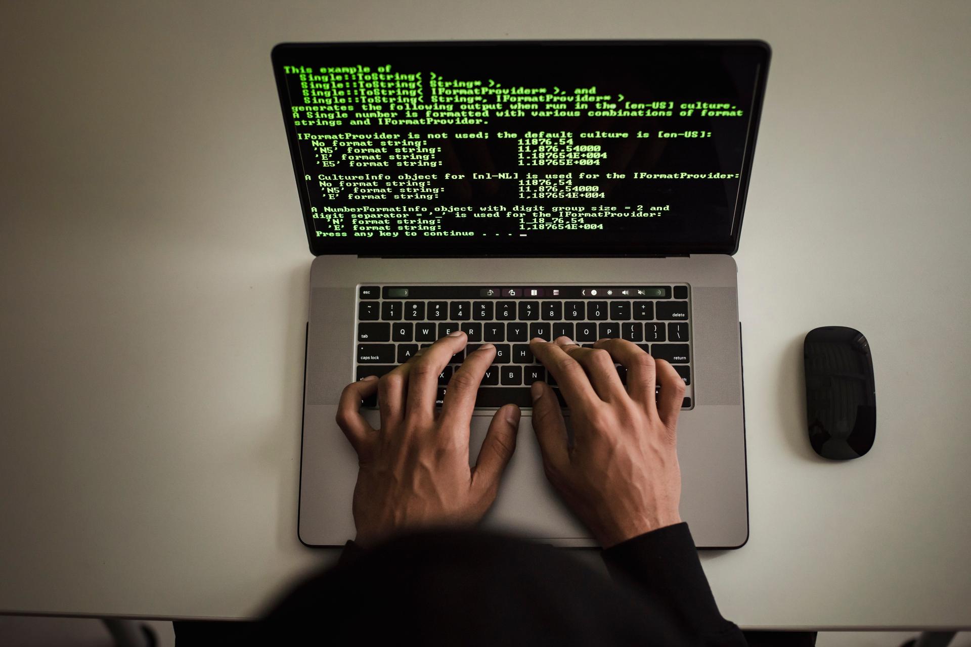Close-up of a software developer typing programming code on a laptop keyboard in a darkened workspace