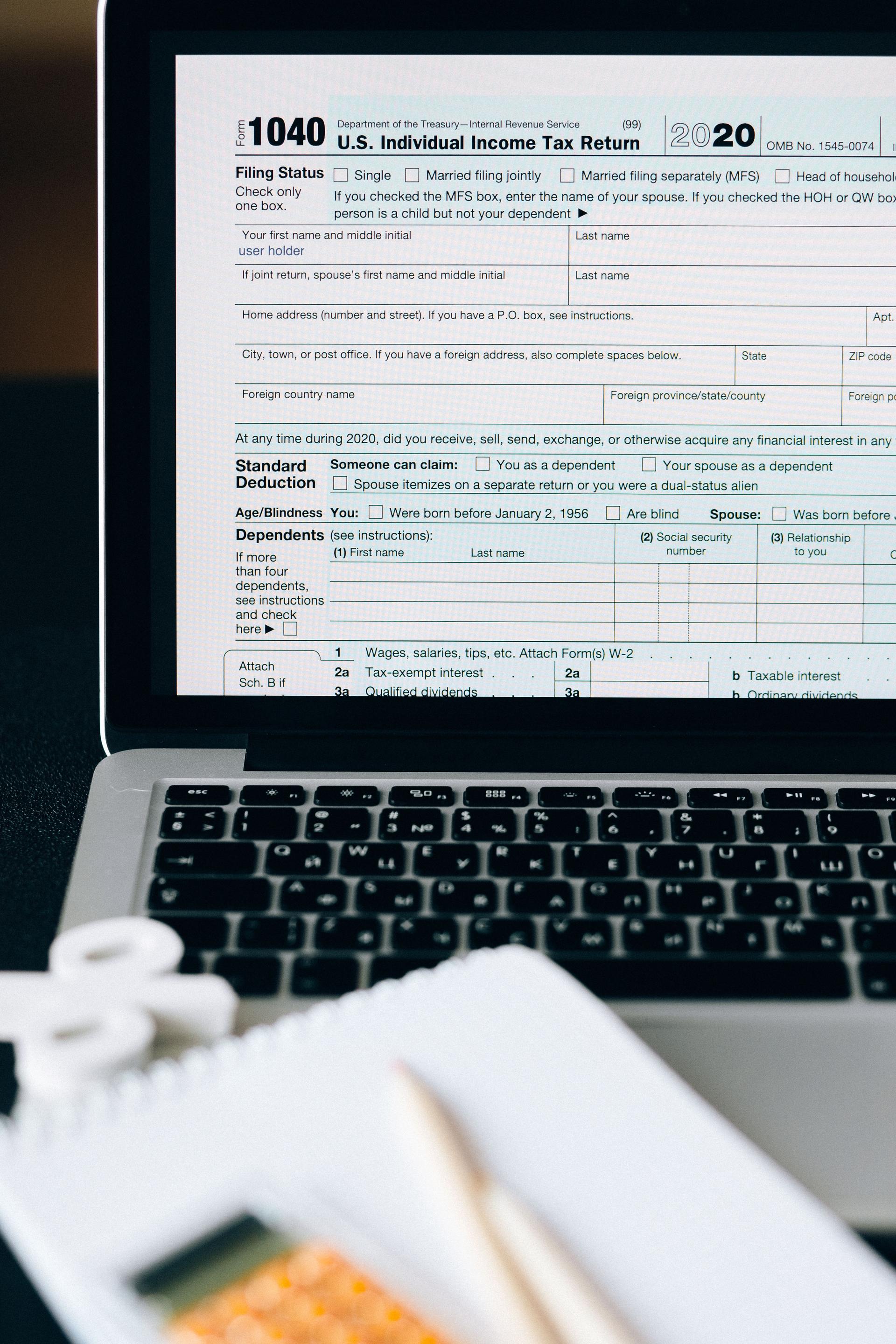 A person filing a tax return online on a laptop beside paperwork and a calculator