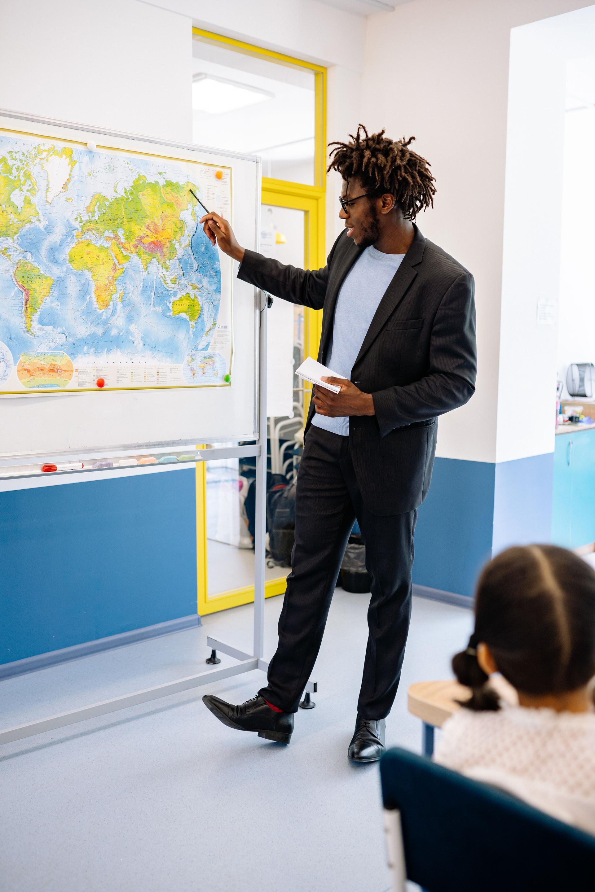 A teacher uses a map to explain world geography to attentive students in a bright classroom