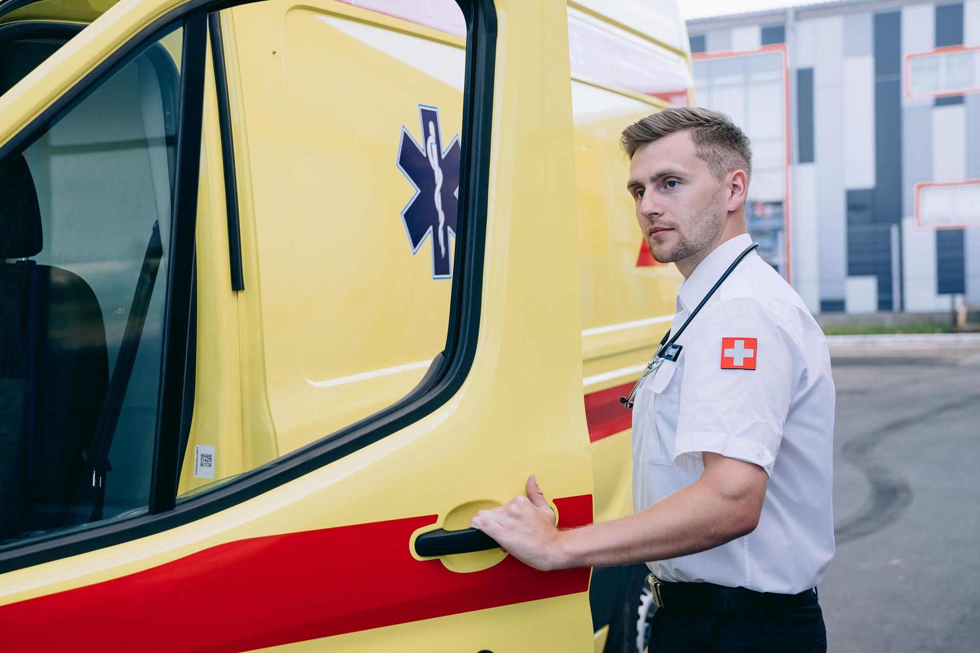 A paramedic in uniform opens the rear door of a yellow ambulance, ready to respond to an emergency call.