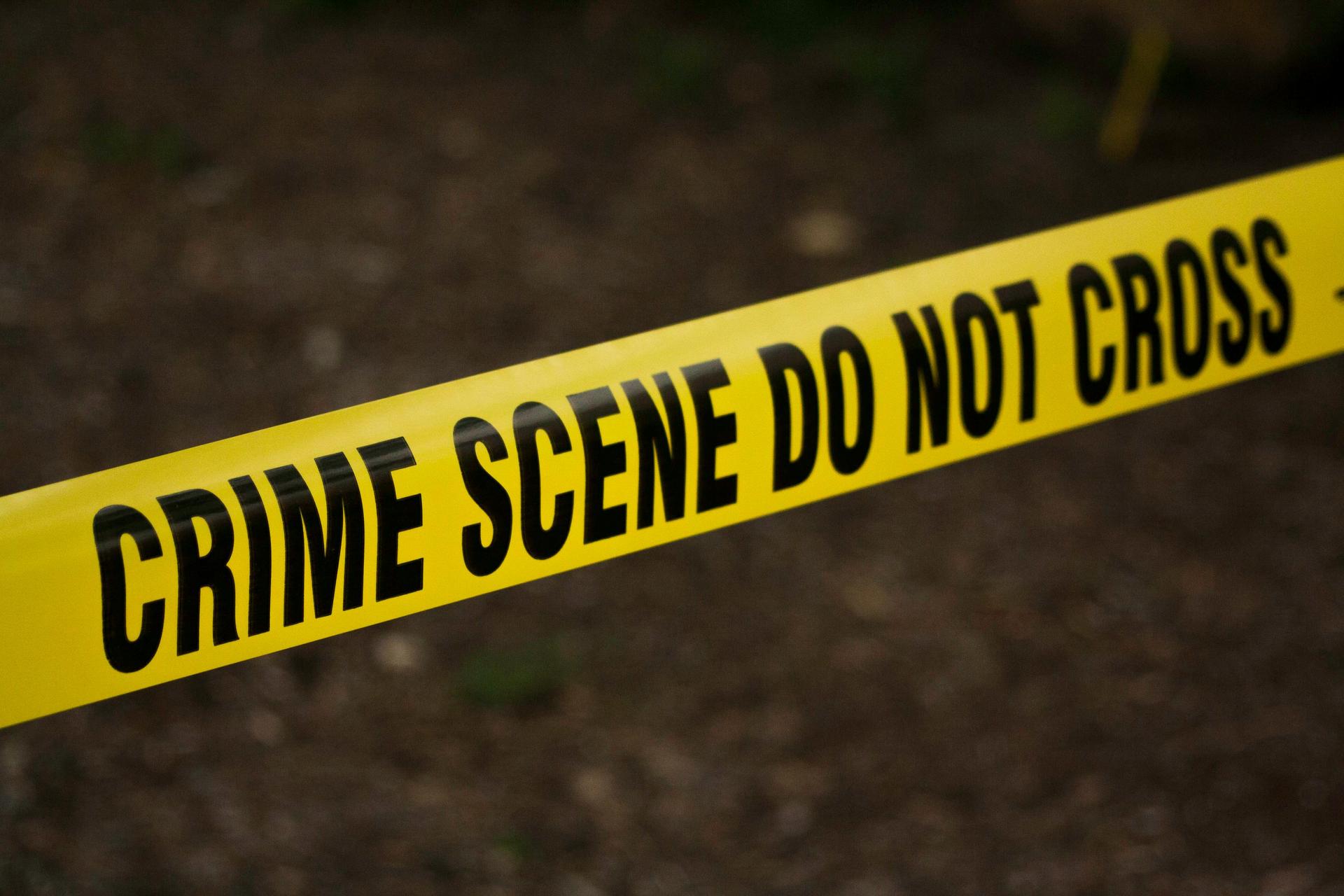 Yellow police crime scene tape printed with Do Not Cross stretched outdoors, marking off an active investigation site.
