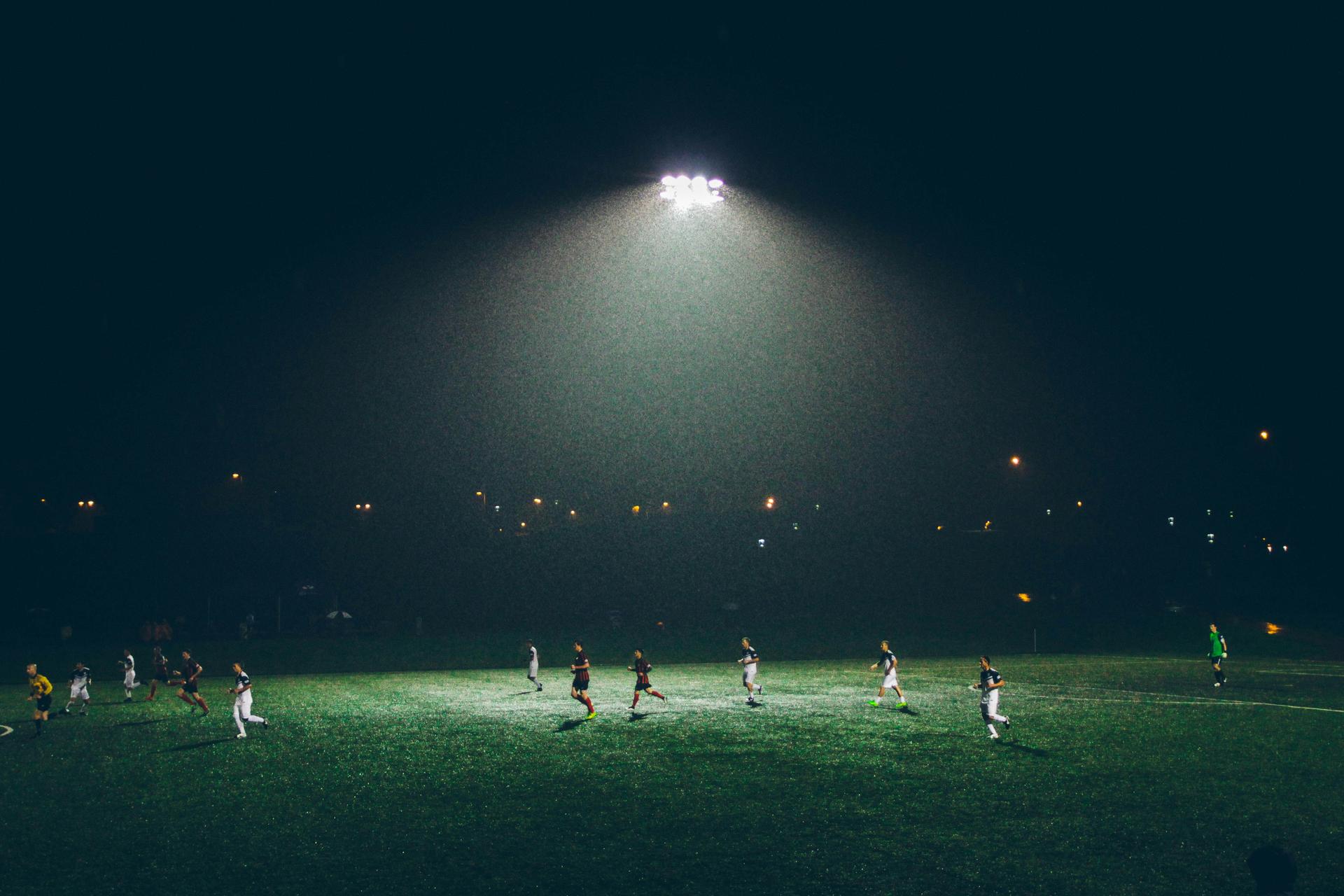 Aerial view of an empty green football pitch with floodlights and empty stands surrounding the field.