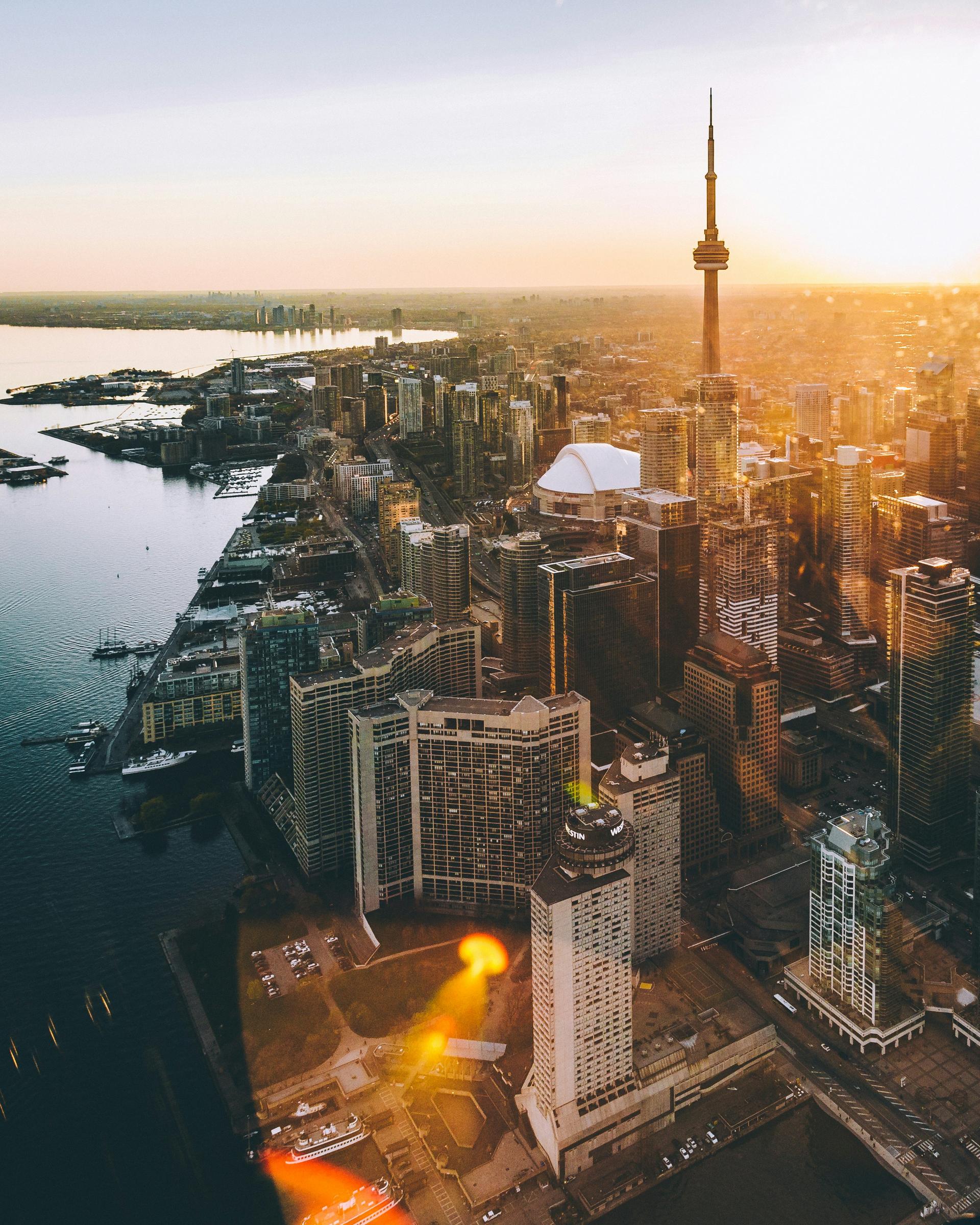Aerial view of the Toronto skyline at sunset, the CN Tower rising above the city beside Lake Ontario.