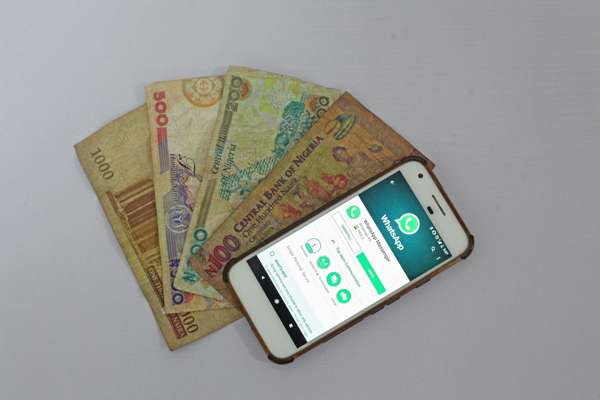 A white smartphone resting beside banknotes on a table, illustrating a mobile-money transfer