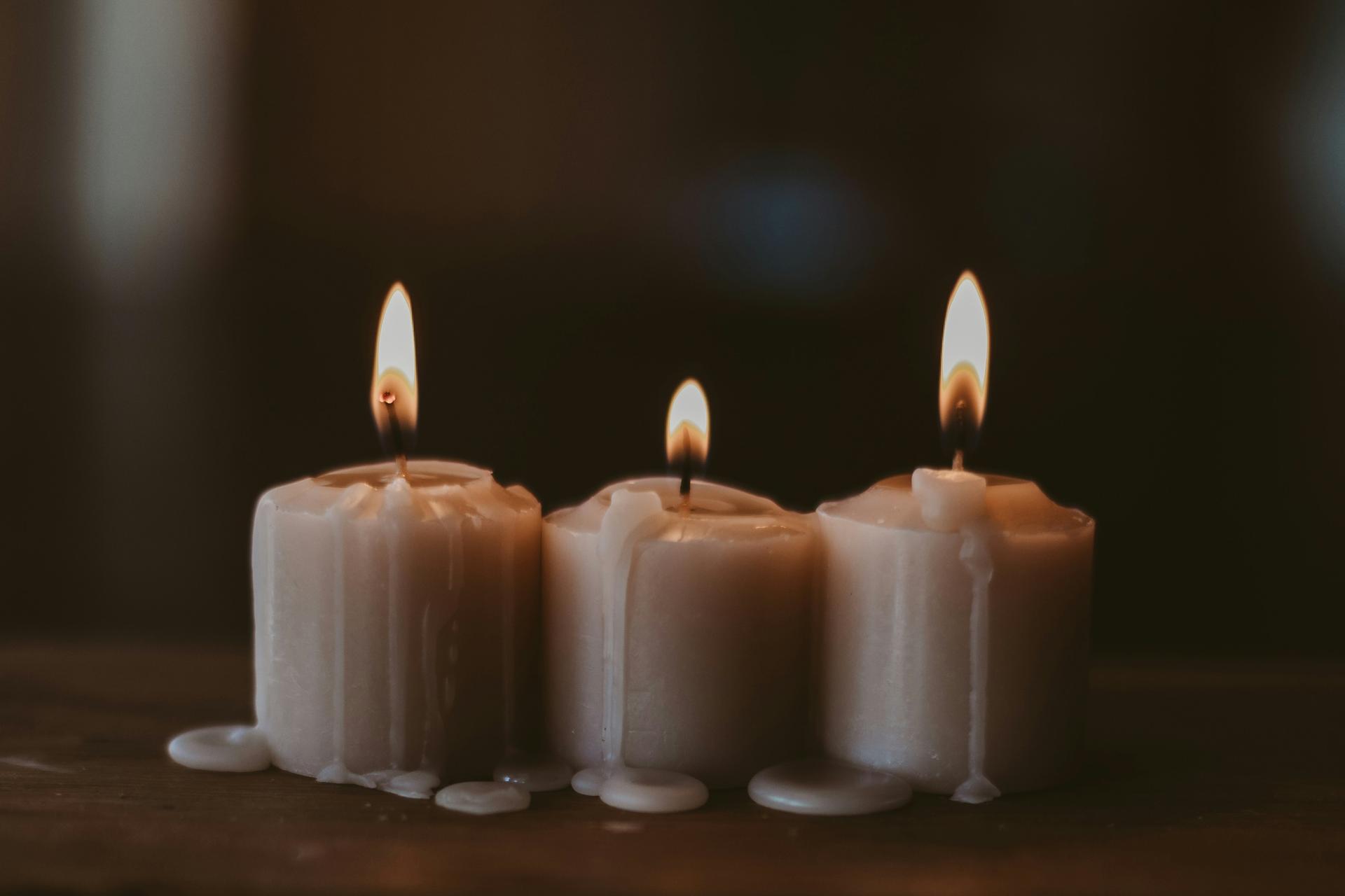 A single lit candle glowing against a dark background, a symbol of mourning and remembrance.