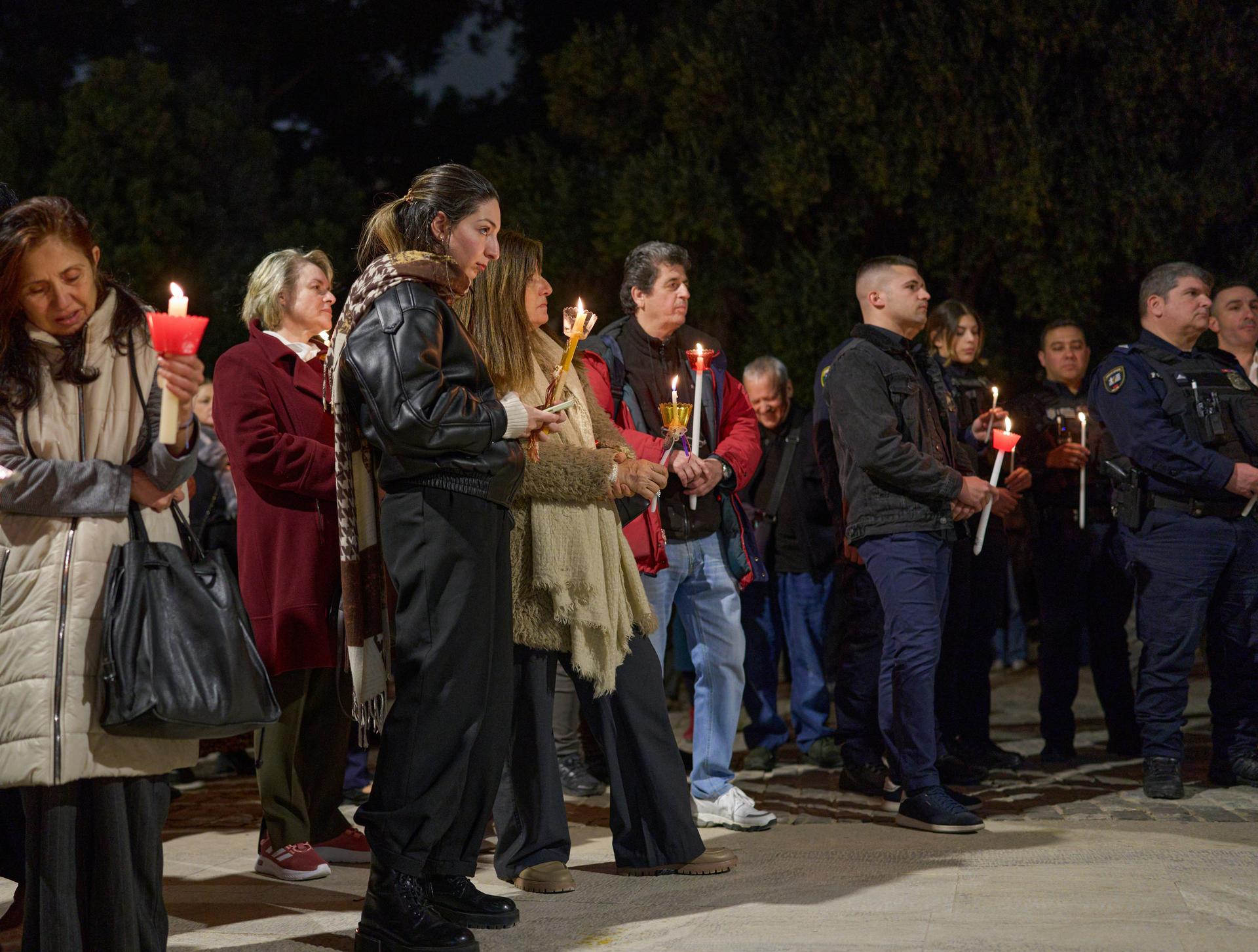 People holding lit candles together at a night-time vigil, gathered in quiet solidarity.