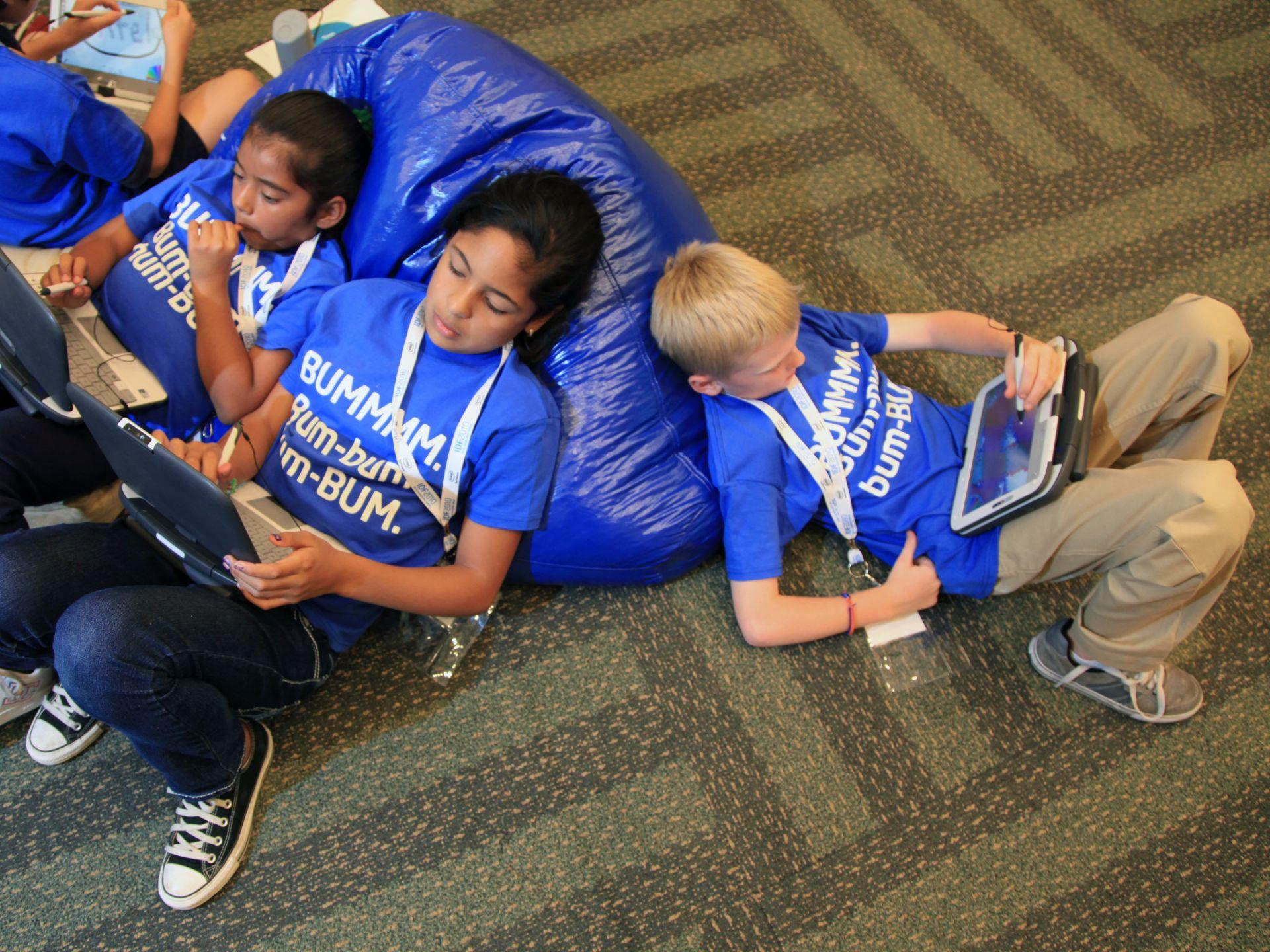 Young children sit together using handheld tablet computers in a classroom setting