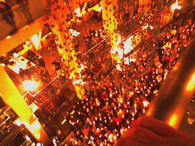 Mourners holding lit candles close together at a nighttime candlelight vigil