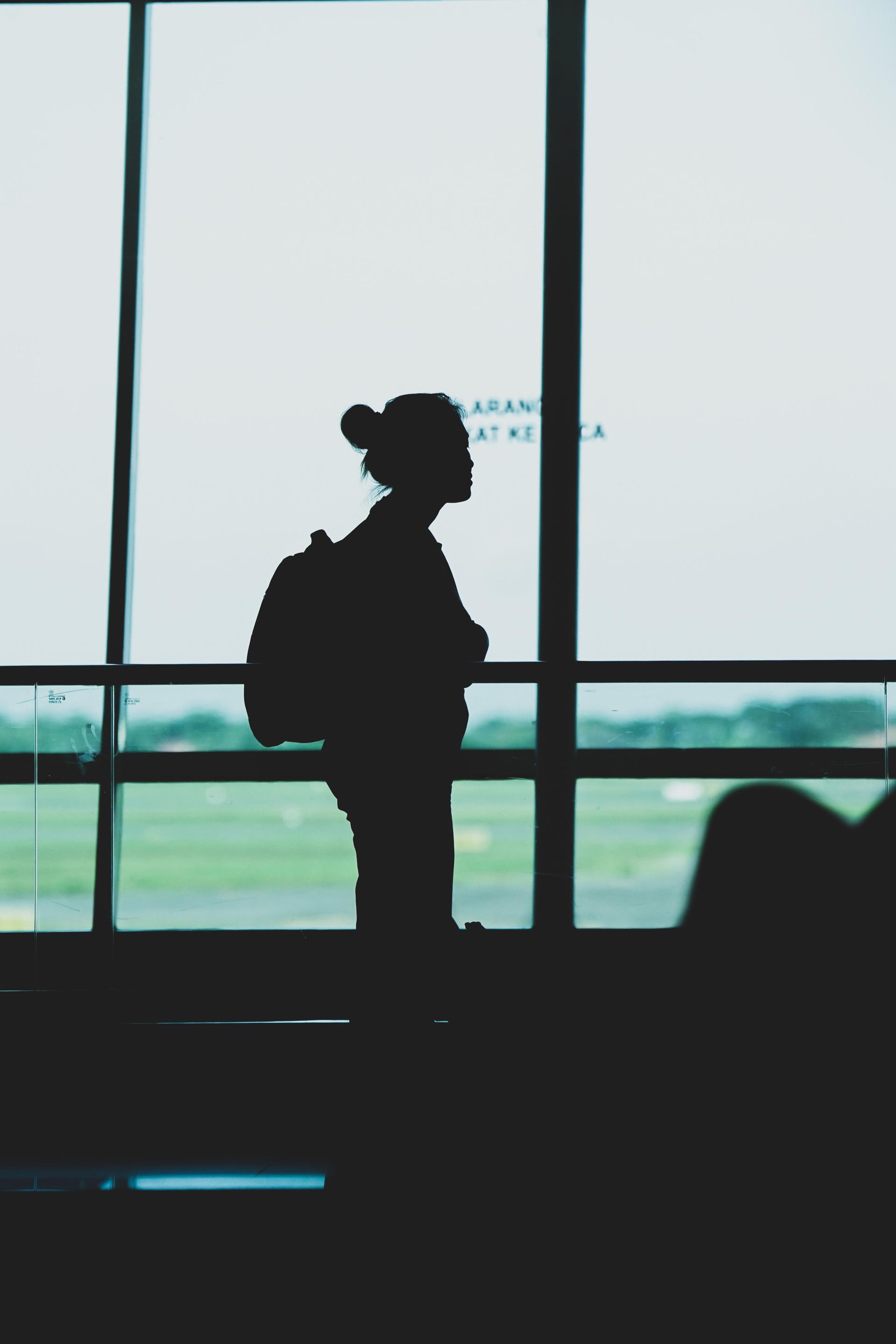 Silhouette of a traveller with a backpack standing in an airport terminal at dusk