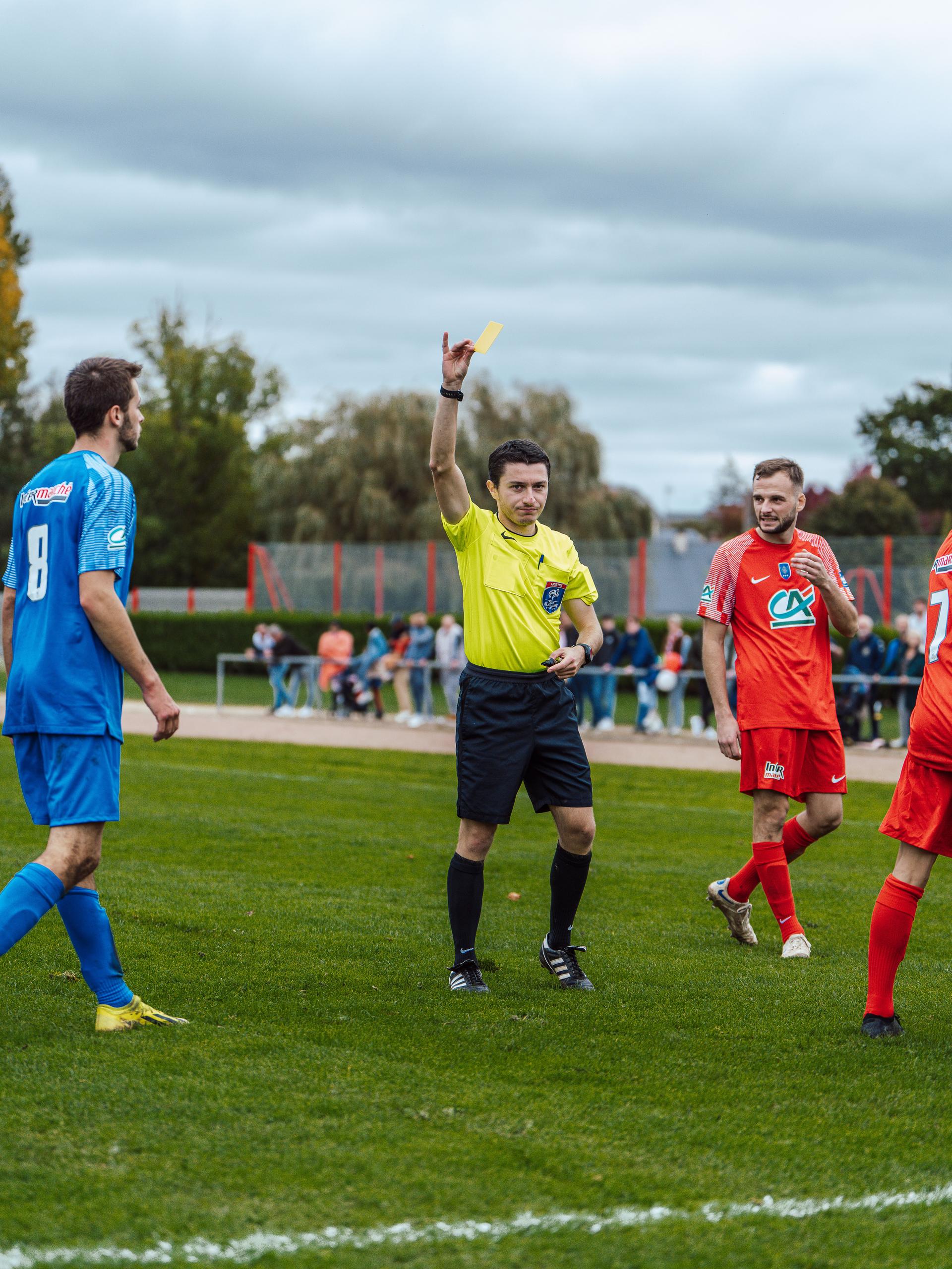 A football referee holds up a card to a player during an outdoor match