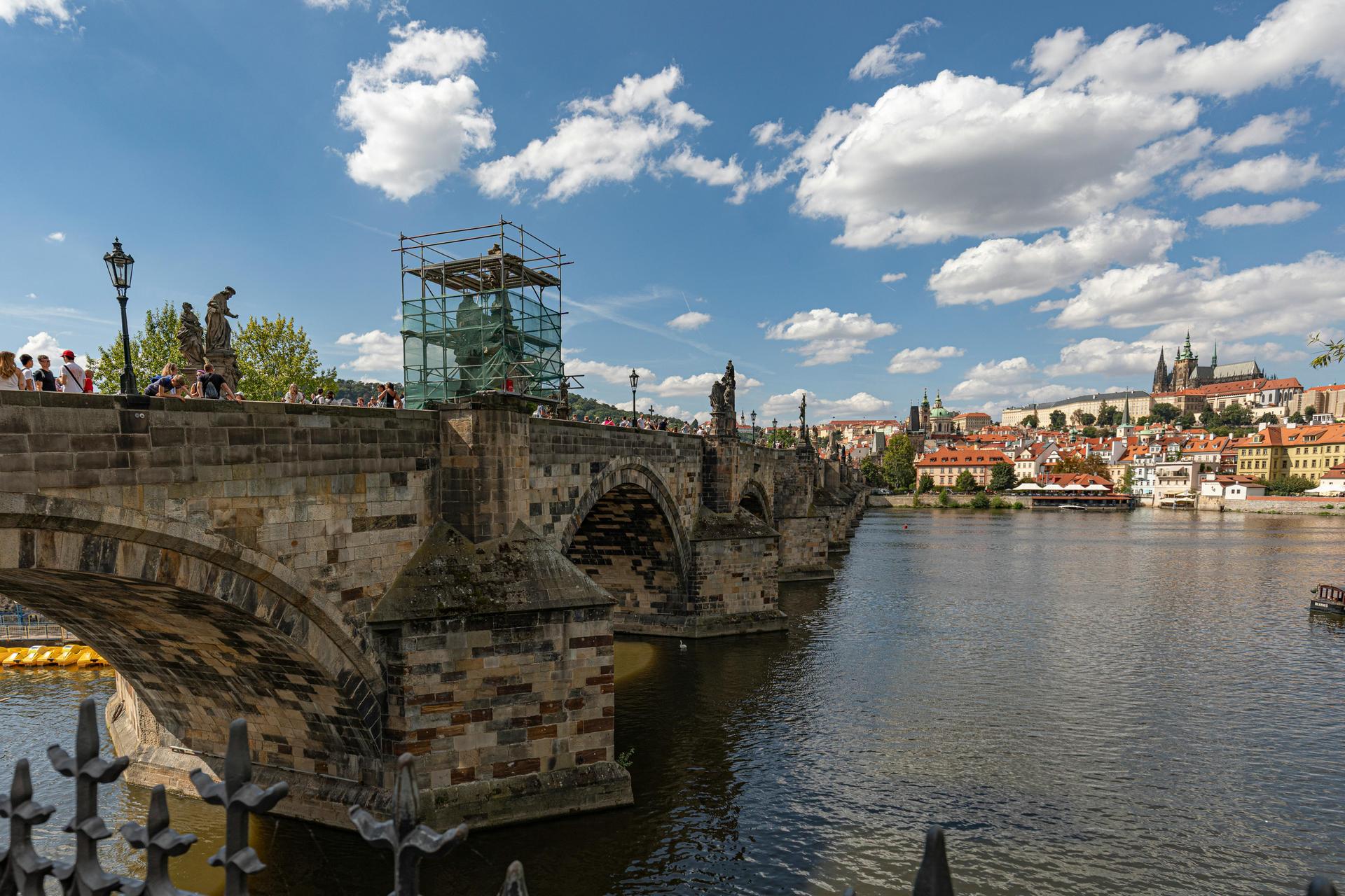 Crowds walk across the Charles Bridge in Prague with the Vltava River and Old Town beyond