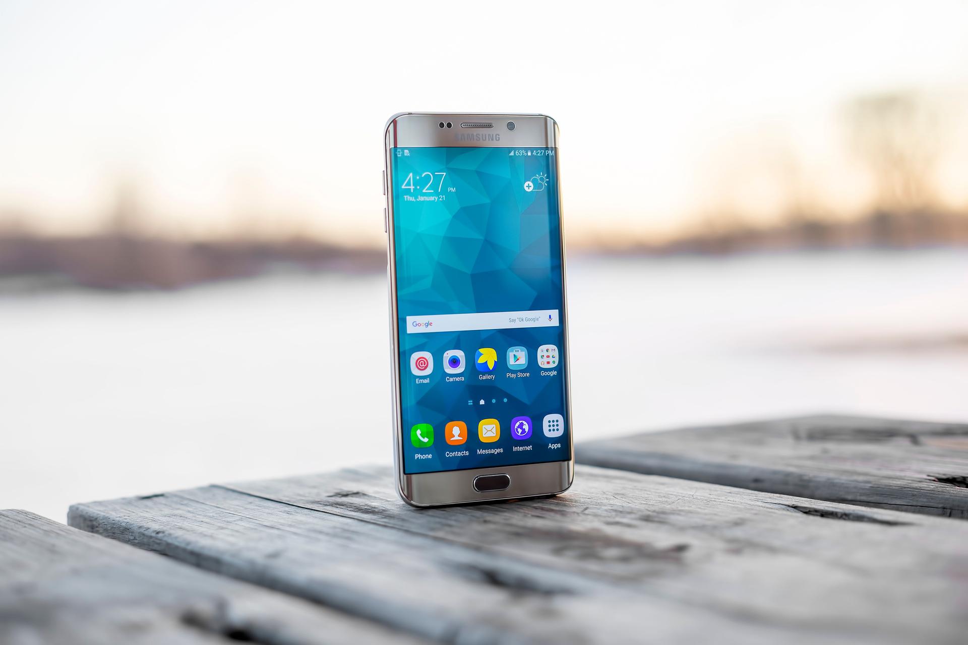 A person holding a modern smartphone in their hands, screen lit