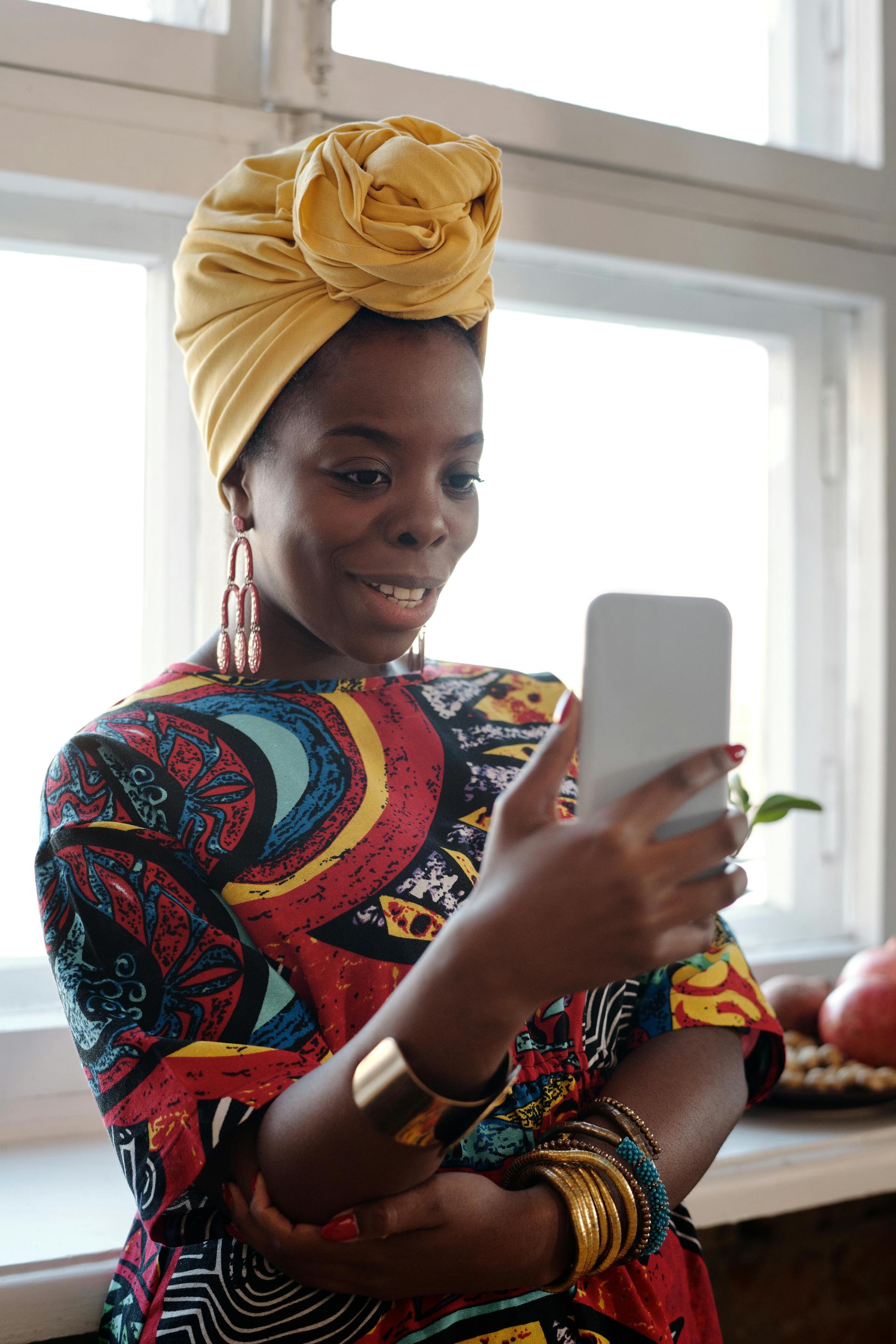 A woman in colorful African attire smiles during a smartphone video call, representing the diaspora-family link that runs through every Kenyan handset.