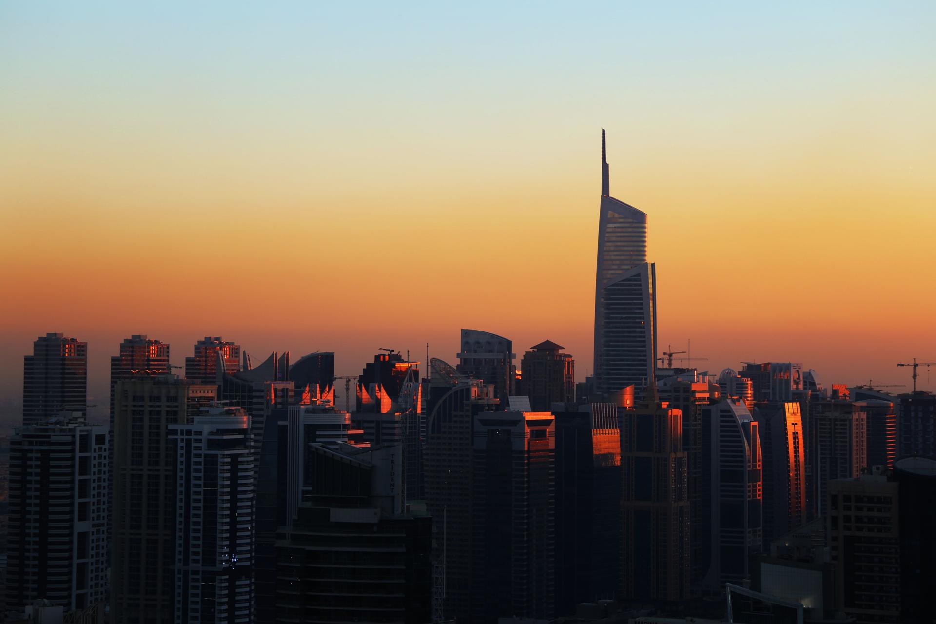 A Gulf city skyline of high-rise towers glowing at sunset, where hundreds of thousands of Kenyan migrants work