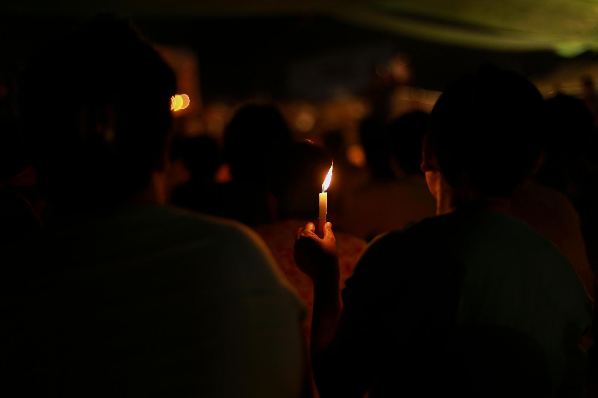 A single candle held in a darkened room, an image of vigil, mourning and quiet reflection.
