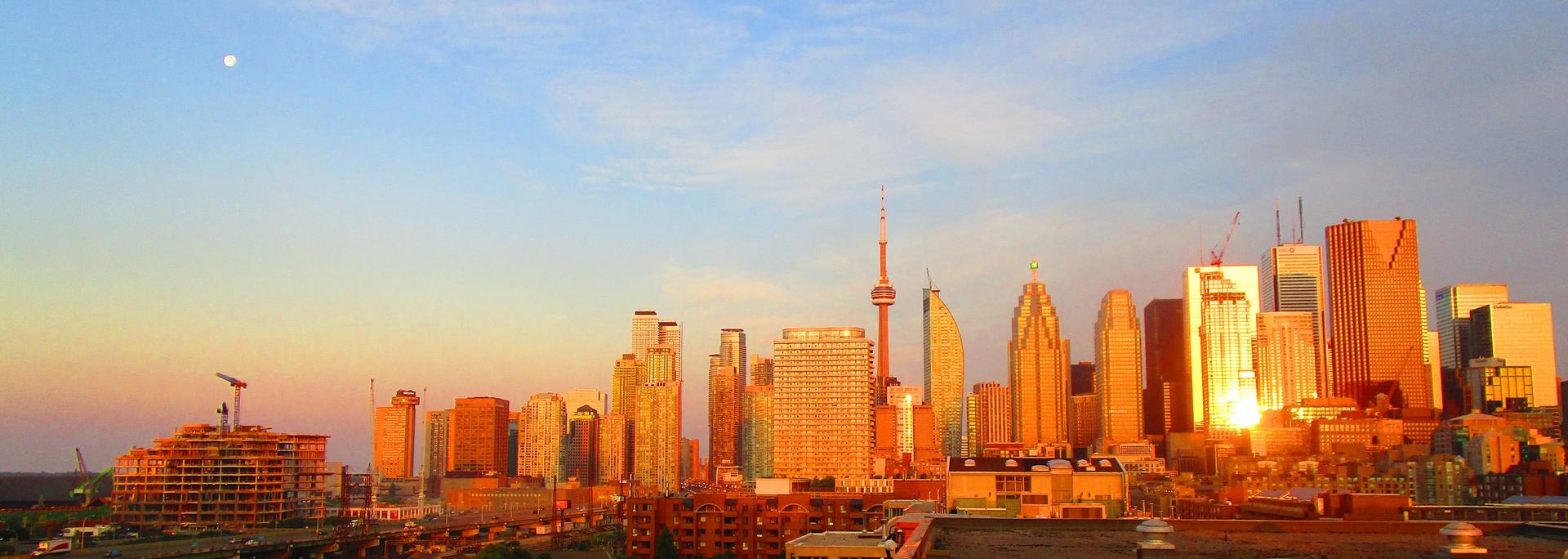 Toronto skyline at dawn with the CN Tower silhouetted against a soft pink and blue morning sky over Lake Ontario