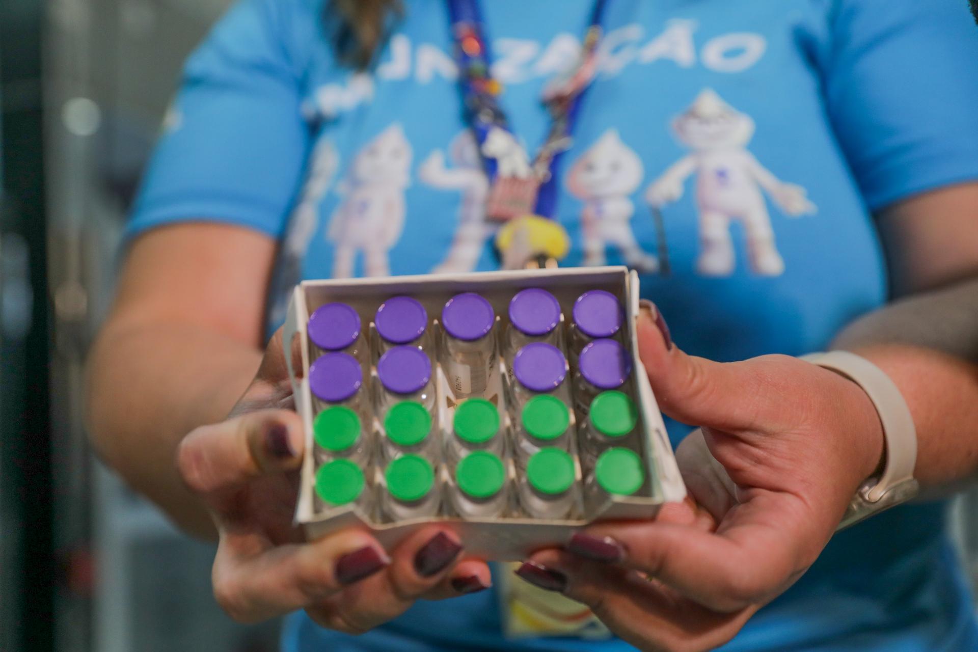 A gloved health worker handles small glass vials of medicine at a vaccination point.