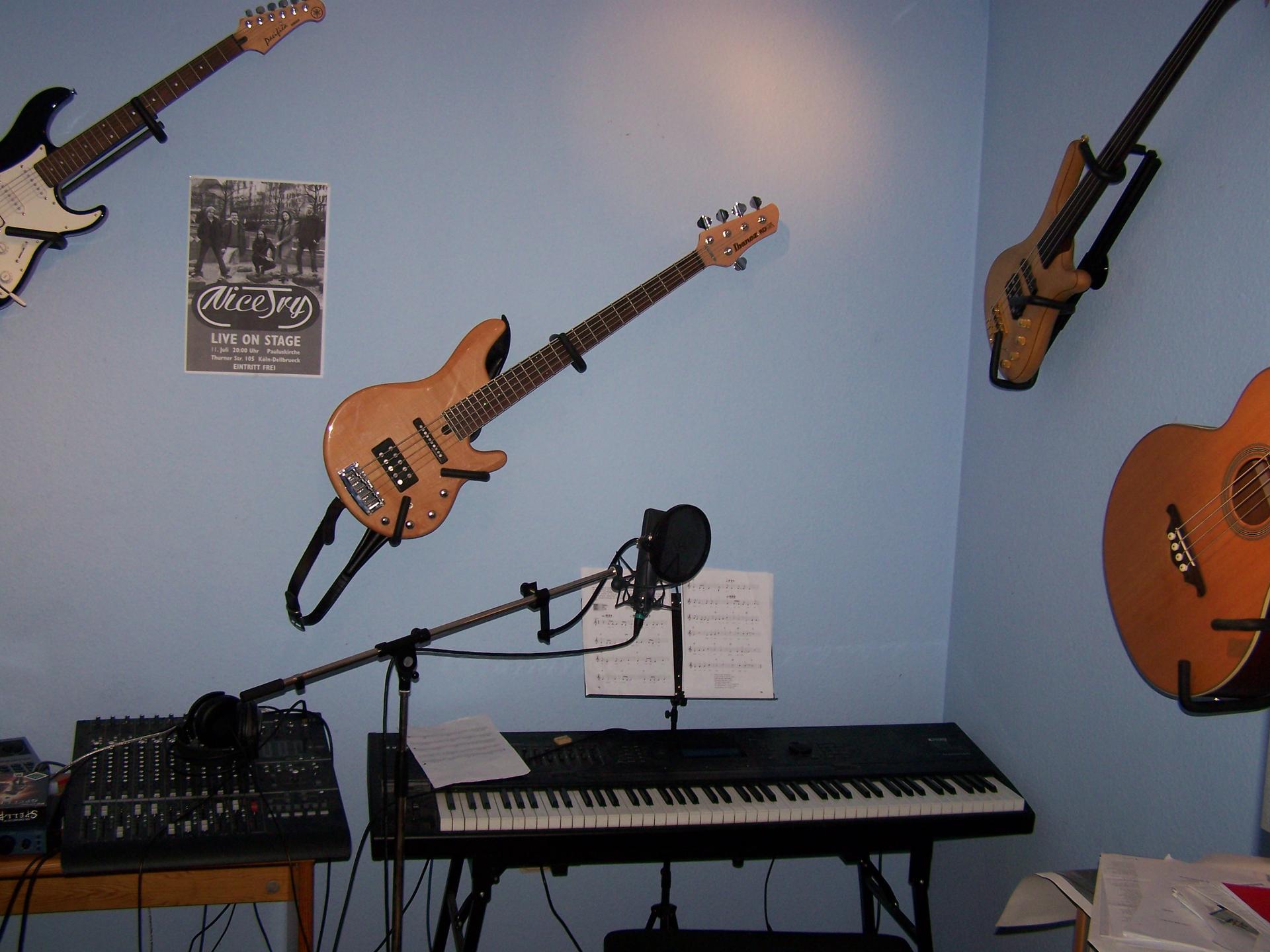 A home recording studio with a microphone and pop shield, mixing gear, keyboard and electric bass guitar.