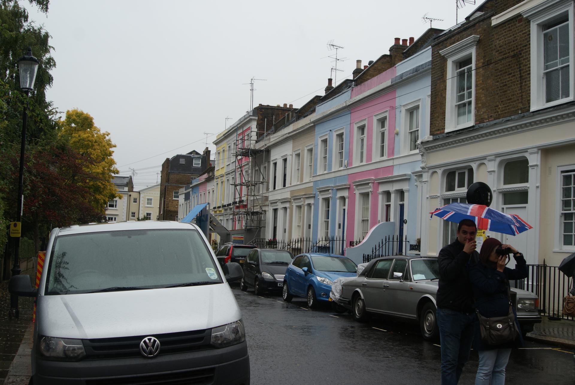 A row of brightly coloured terraced houses along a London residential street under a clear sky.