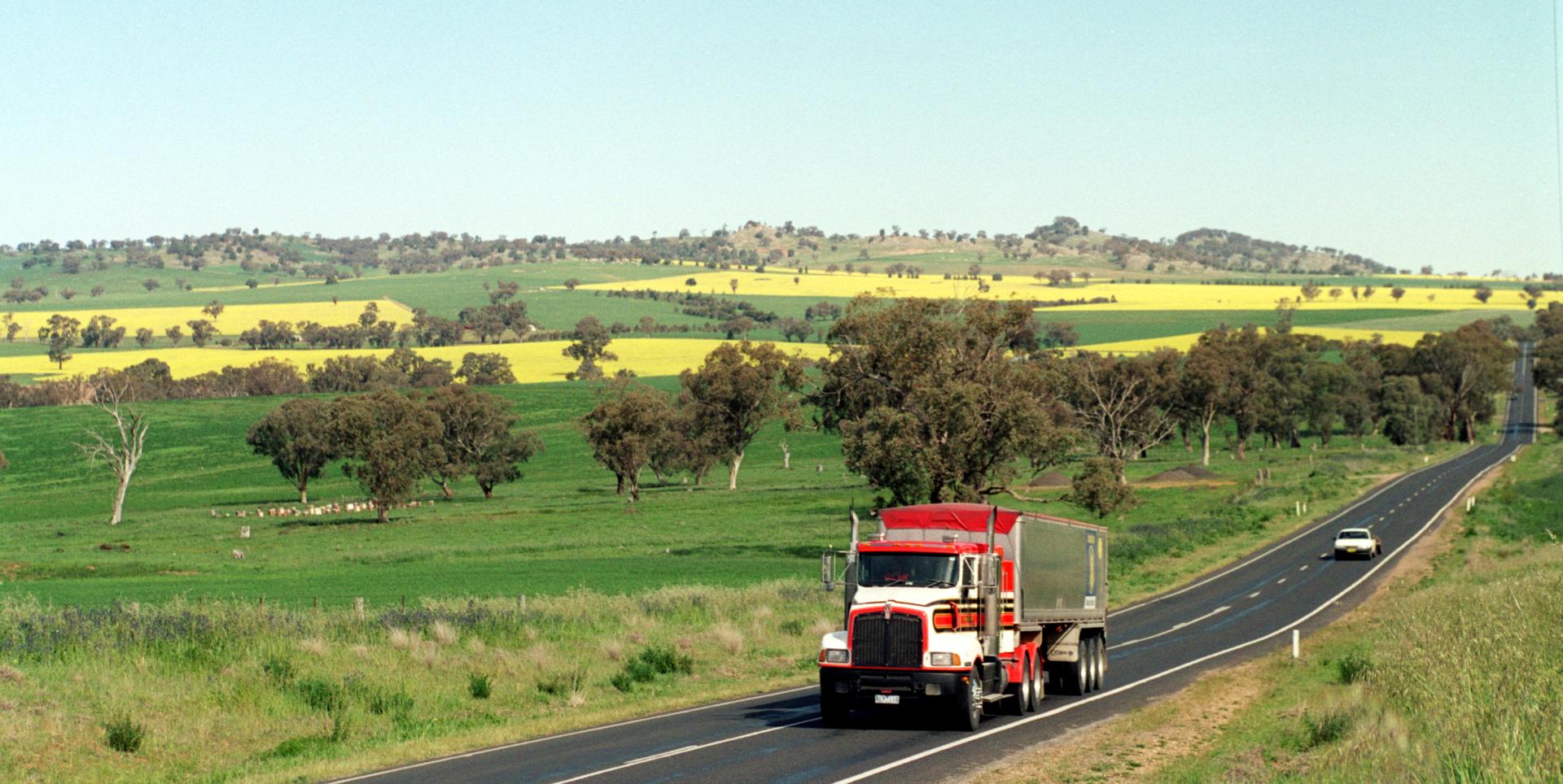 A semi-trailer truck travels along a rural highway under an open sky