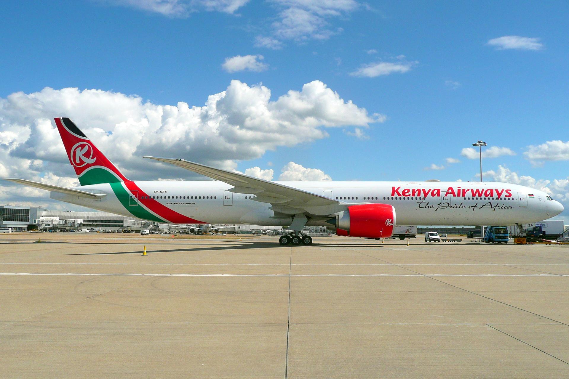 A Kenya Airways Boeing 777-300 on the tarmac at London Heathrow Airport under an overcast sky.