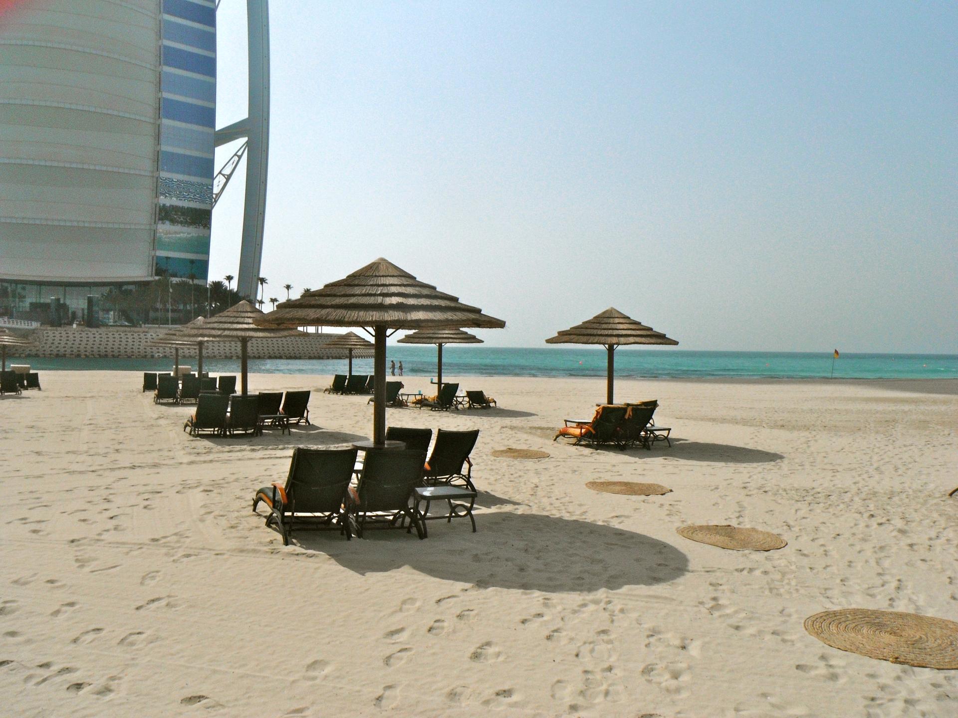 Sunbathers and calm turquoise water along the shoreline of Dubai's Jumeirah Beach on a bright, clear day.