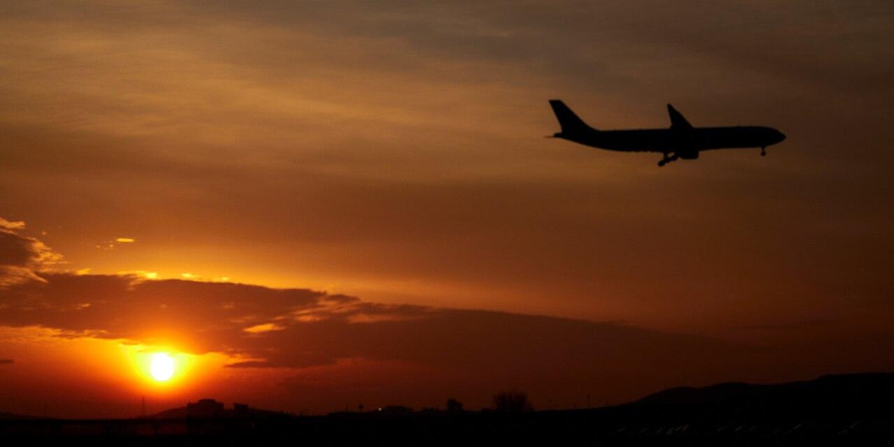 A passenger jet silhouetted against an orange sunset sky at an airport runway