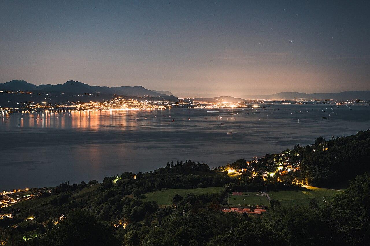Évian-les-Bains glows at night across Lake Geneva, seen from the Lavaux vineyards on the Swiss shore.