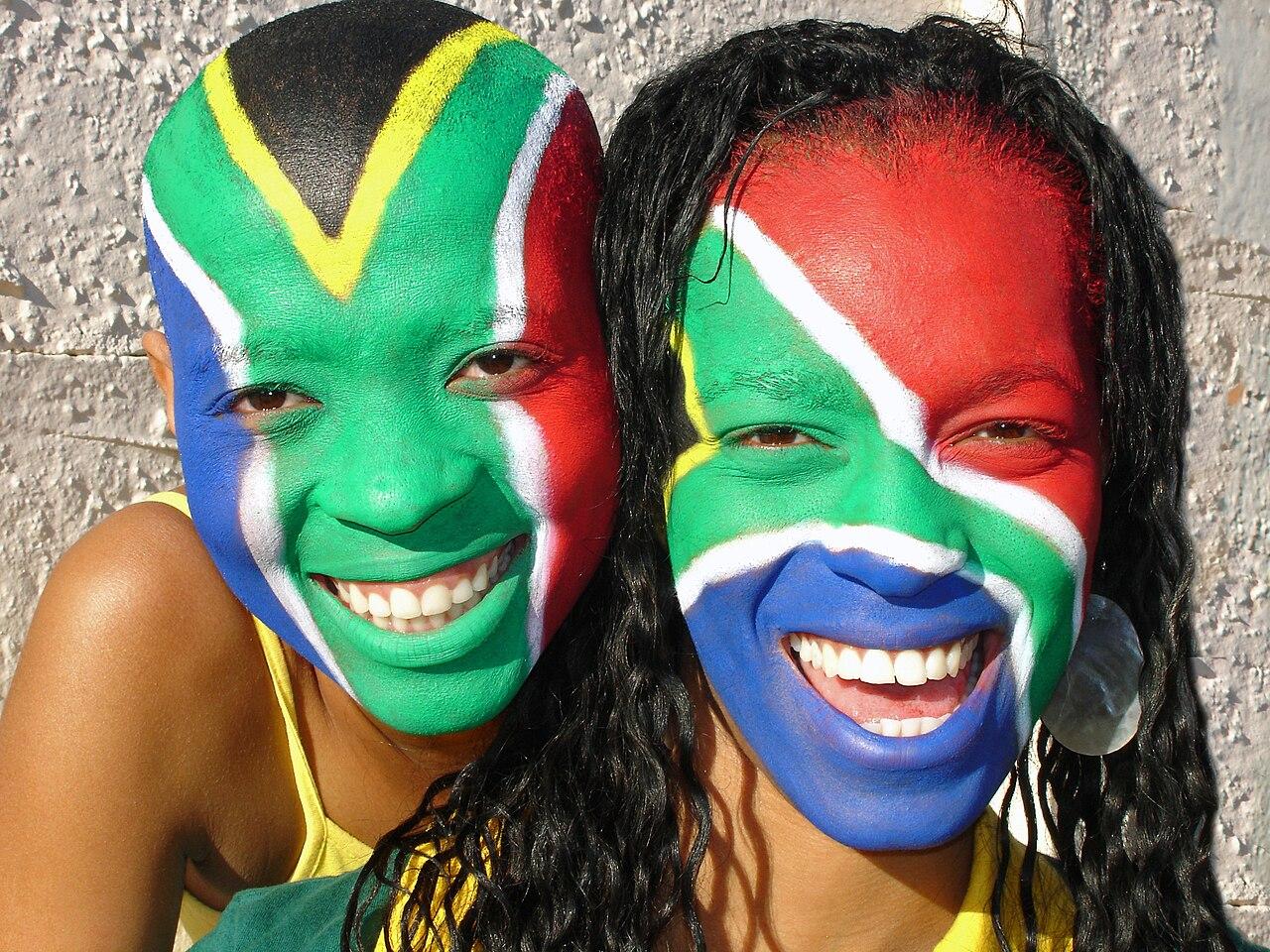Football supporters in team colours wave flags and cheer in a packed World Cup stadium crowd.