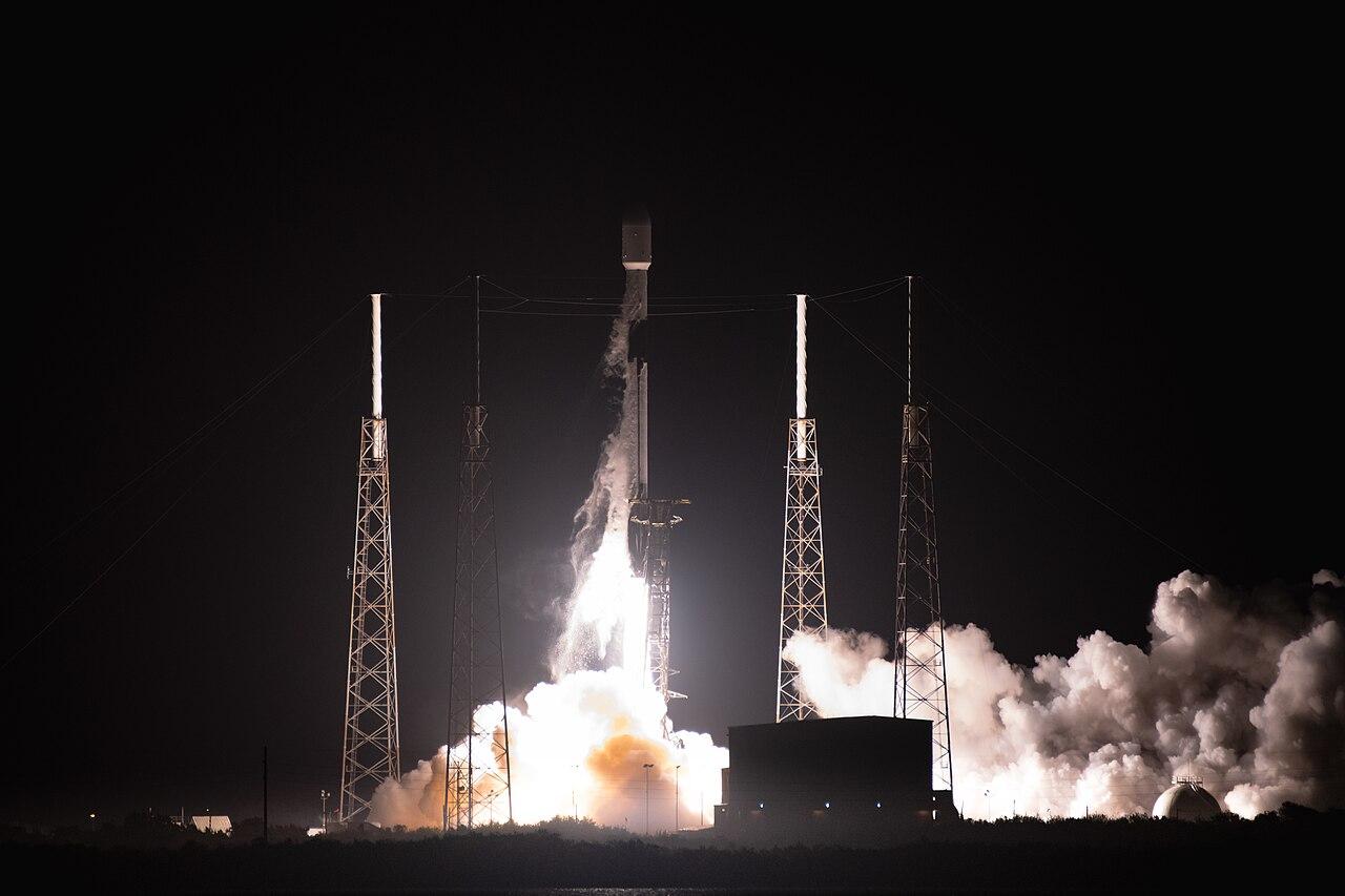 A SpaceX Falcon 9 rocket carrying Starlink satellites lifts off at dusk, leaving a bright trail across the evening sky.