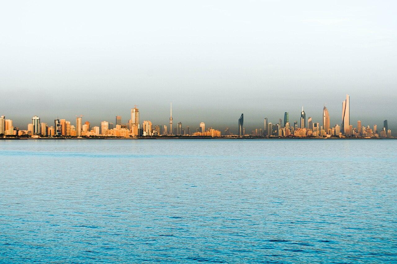 Kuwait City skyline with high-rise towers under a hazy Gulf sky, seen from across the bay