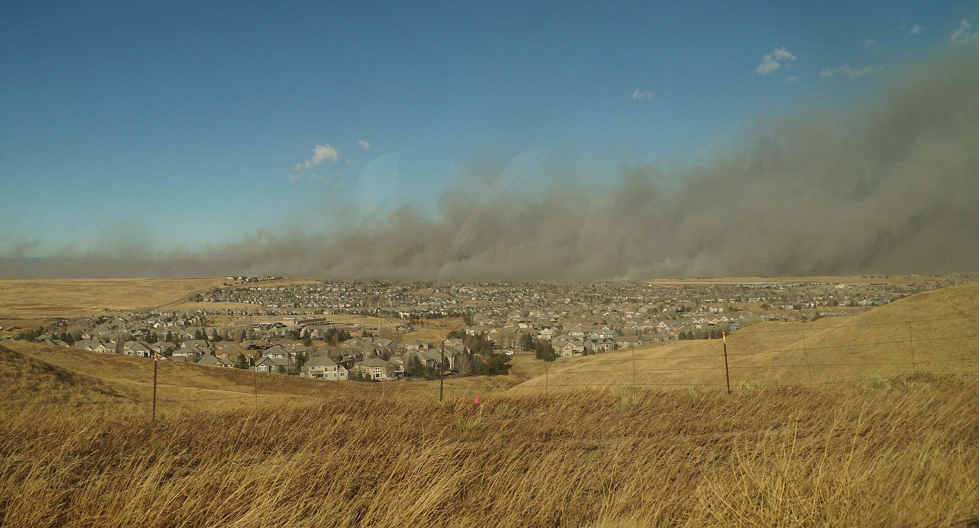 A wall of grey wildfire smoke rises over homes and open ground in Superior, Colorado.