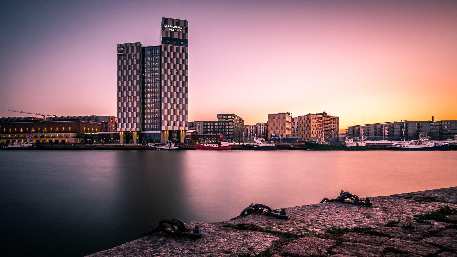 Sunset over the Helsinki, Finland waterfront skyline, with rooftops and harbour buildings beneath a warm evening sky.