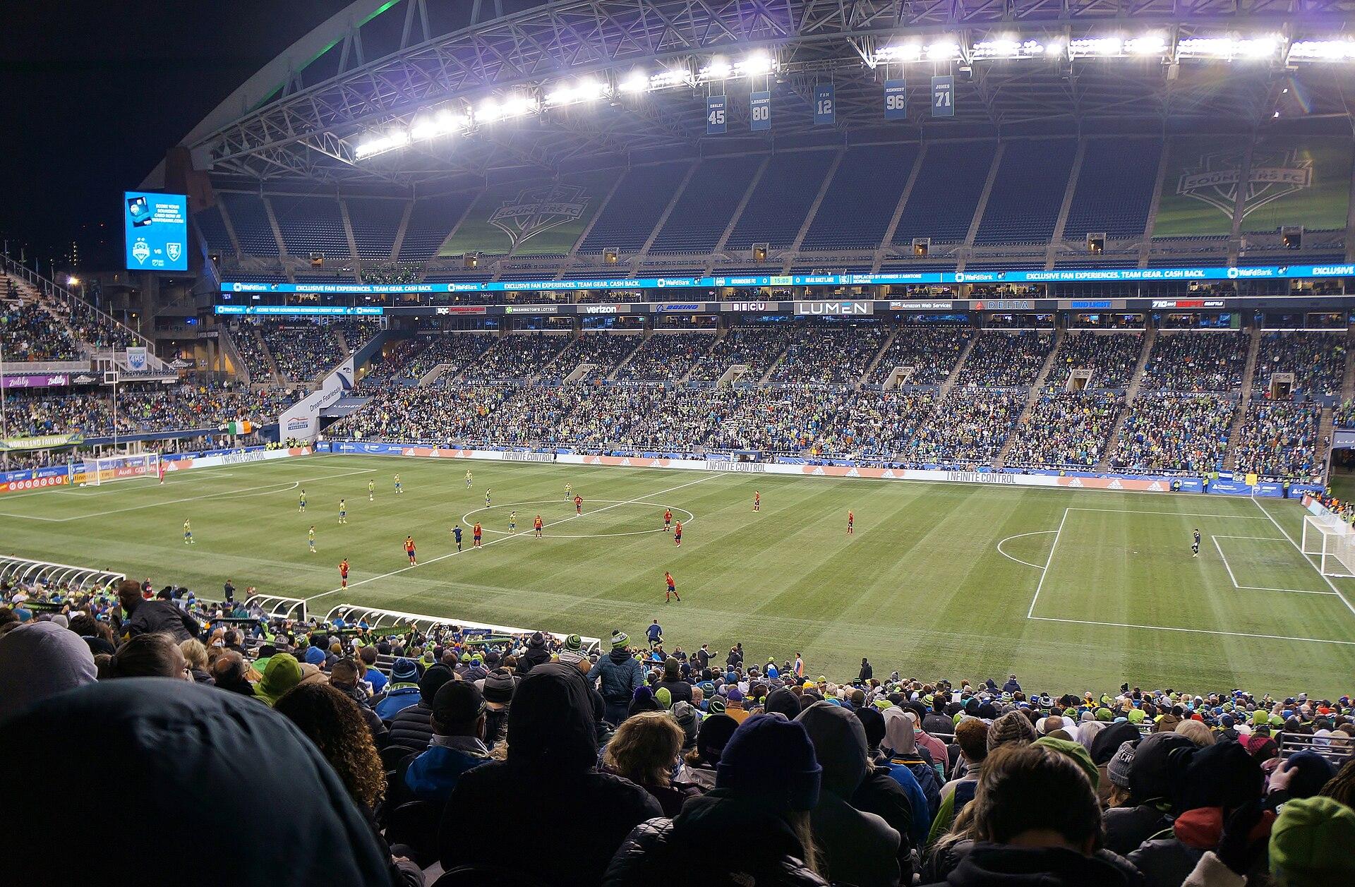 A packed Lumen Field stadium in Seattle during an evening professional soccer match, fans filling the stands