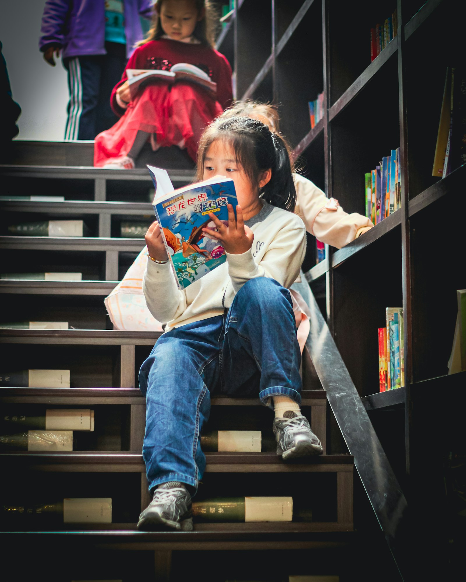 A young girl reads a book alone on a flight of library stairs, illustrating the long road of solitary preparation behind a National Spelling Bee qualifier.