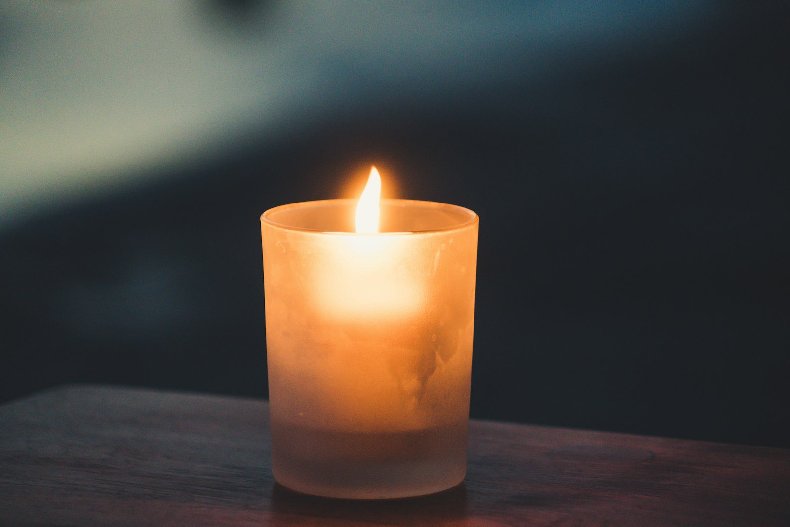 A single lit tea light glows in soft, low light against a dark wooden surface.