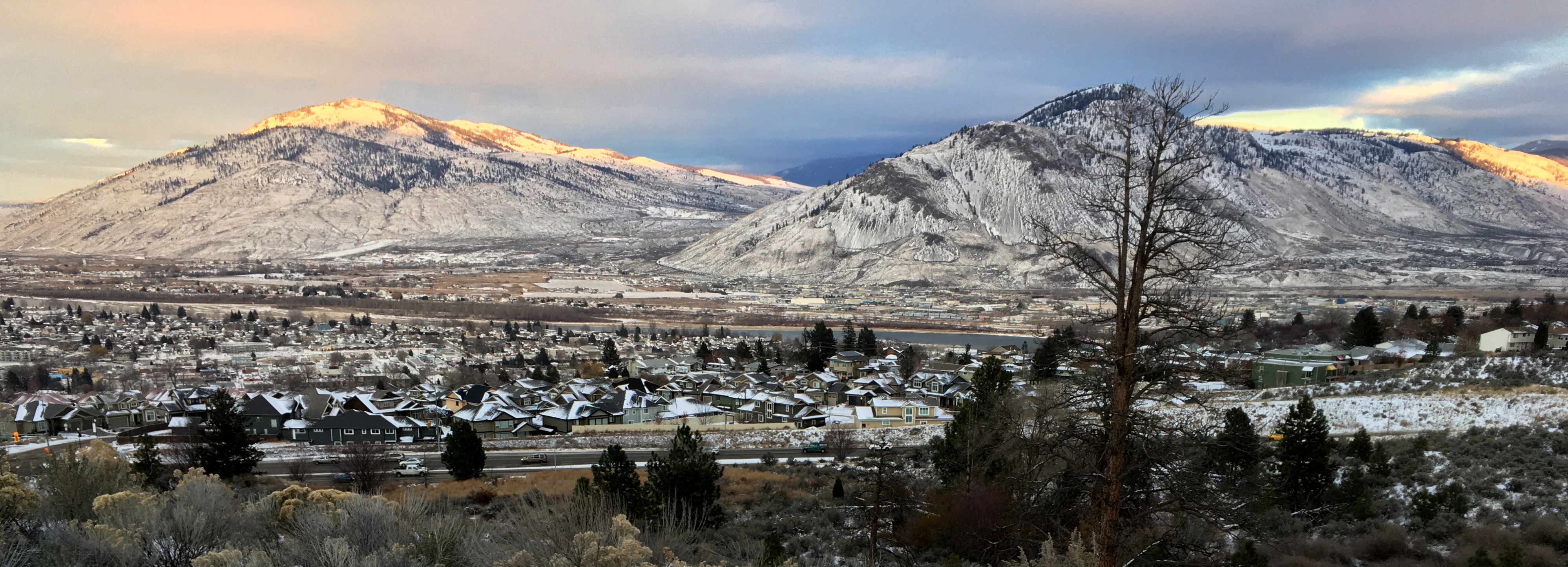 A wide-angle view of two mountains framing the confluence of the North and South Thompson Rivers at Kamloops, British Columbia, on a clear afternoon